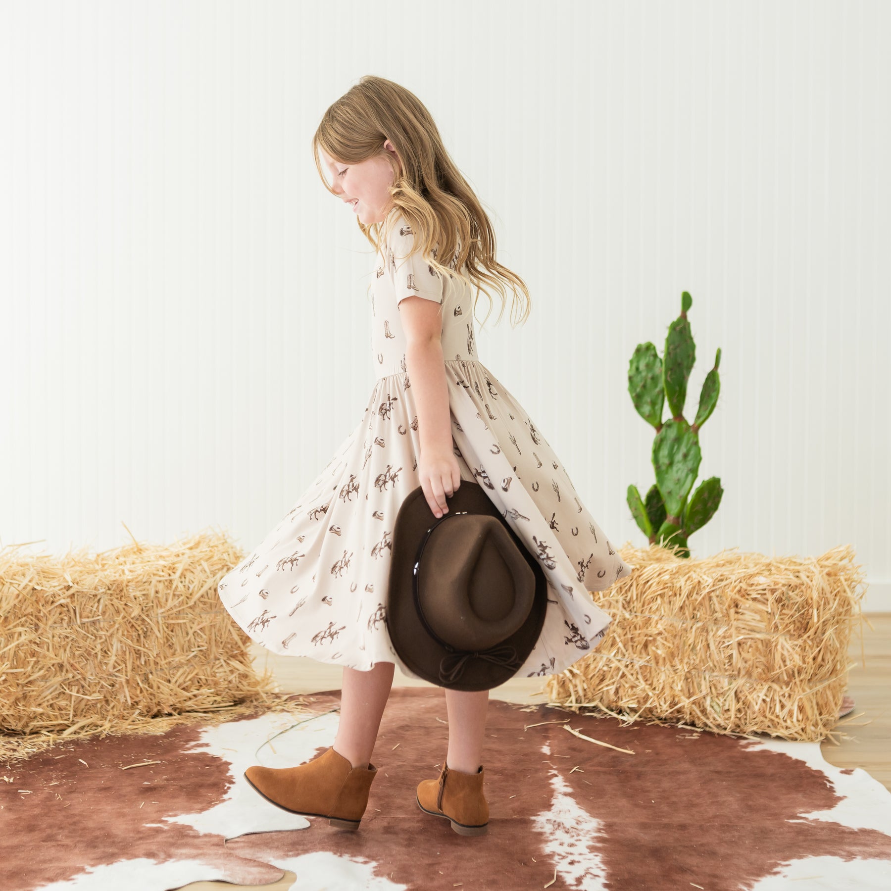 Young girl twirling in a Twirl Dress in Classic Cowboy with a cowboy hat in one hand