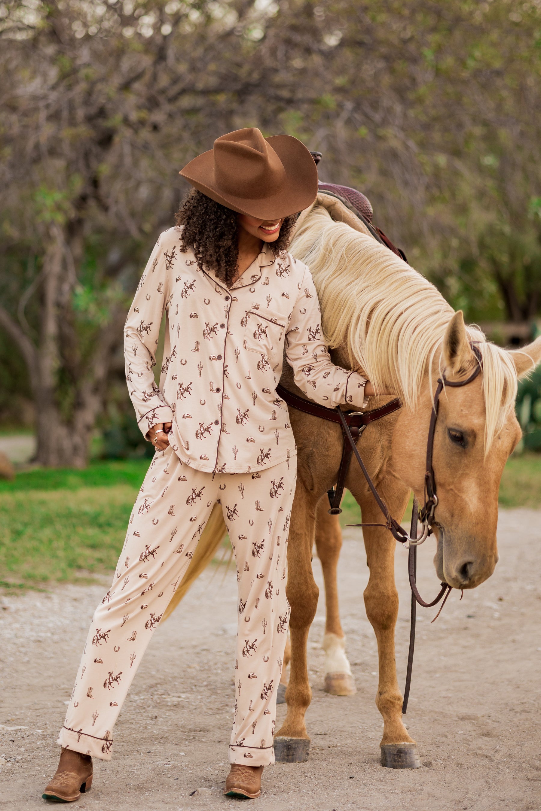 Female model wearing the Long-Sleeved Women's Pajama Set in Classic Cowboy and cowboy hat standing beside a real horse
