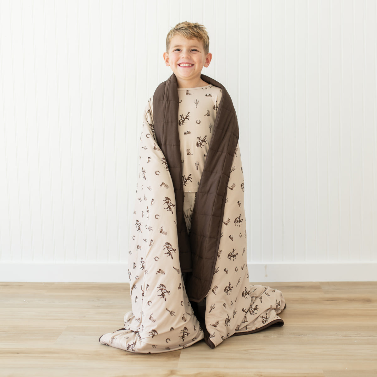 Young smiling boy standing with the Youth Blanket in Classic Cowboy 2.5 around his shoulders in front of a white paneled wall