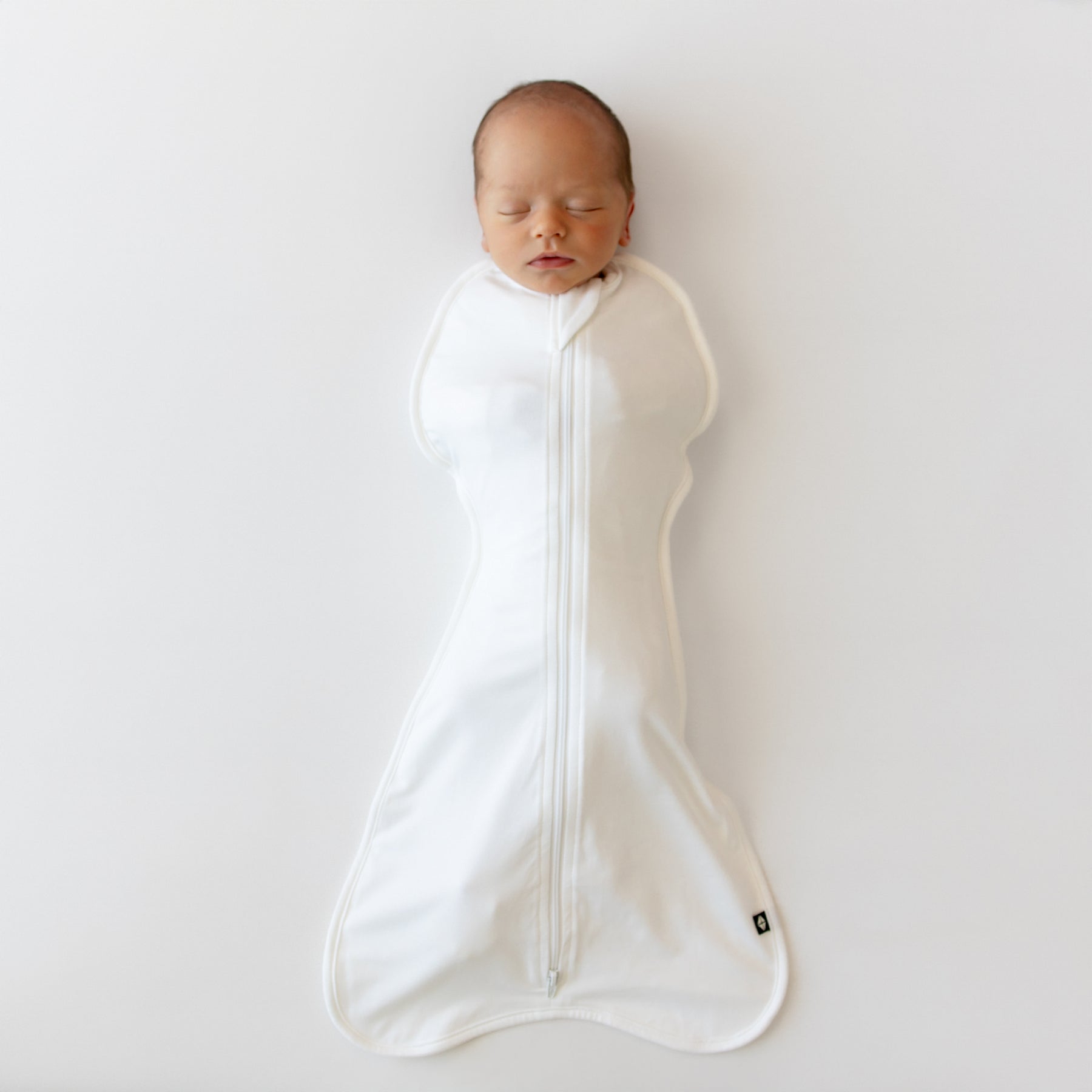 Newborn baby swaddled in a white swaddle on a plain background
