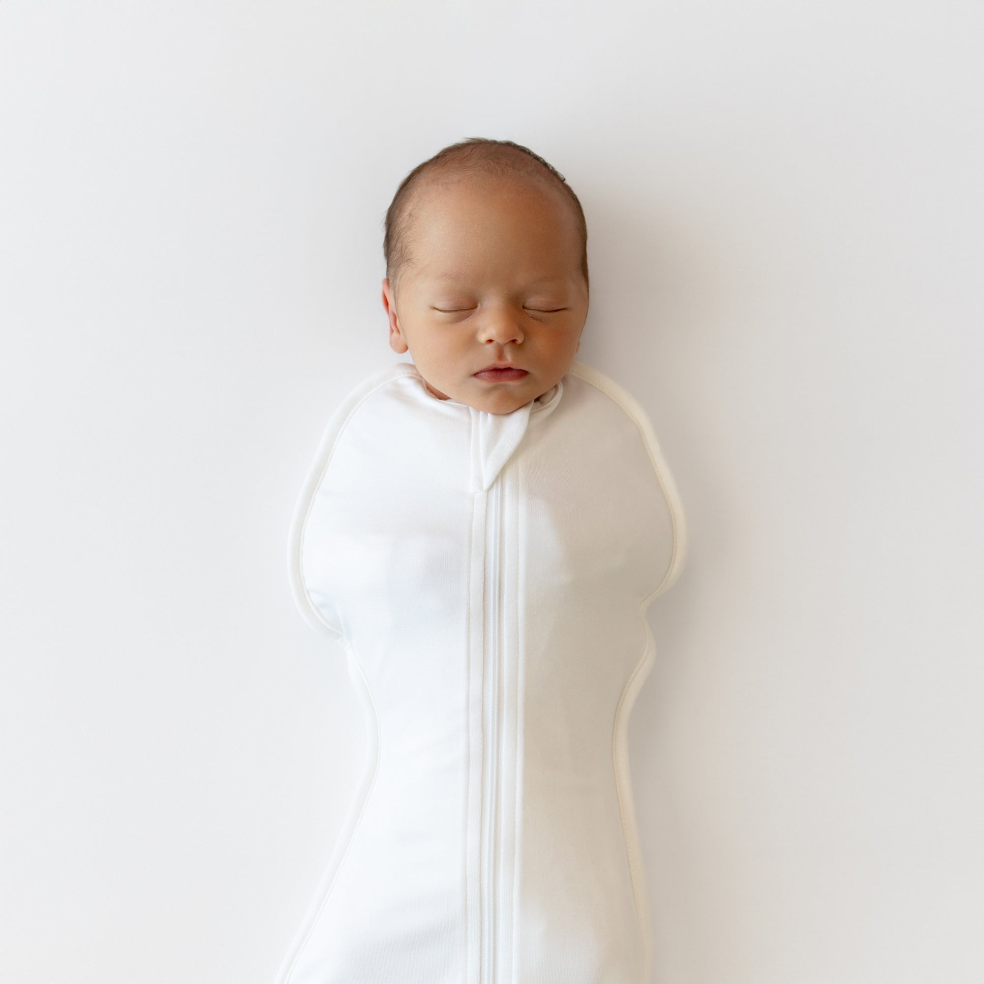 Newborn baby sleeping peacefully in a white swaddle on a light gray background
