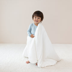 Toddler wrapped in a Toddler Blanket in Cloud 1.0 TOG while wearing a Long Sleeve Pajama Set in Fog