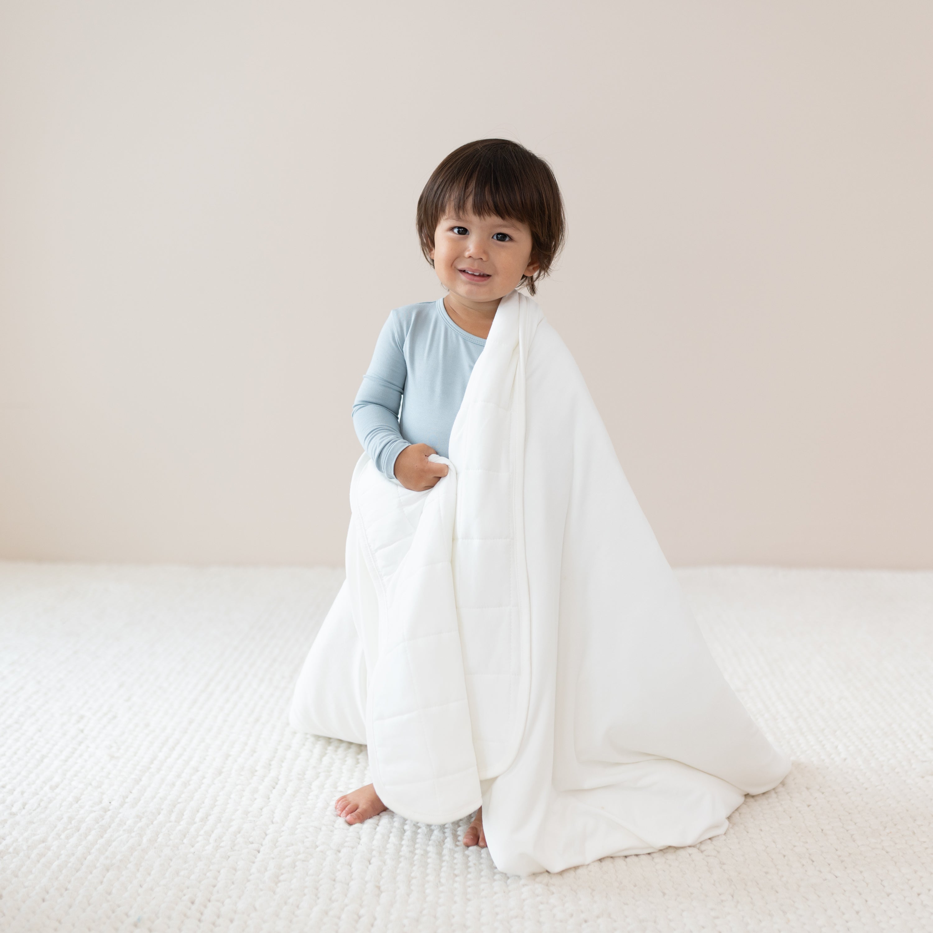 Toddler wrapped in a Toddler Blanket in Cloud 1.0 TOG while wearing a Long Sleeve Pajama Set in Fog