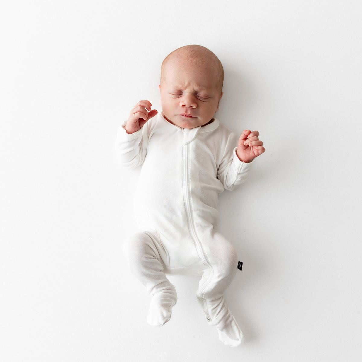 Baby wearing a buttery soft white zippered bamboo footie on a white background