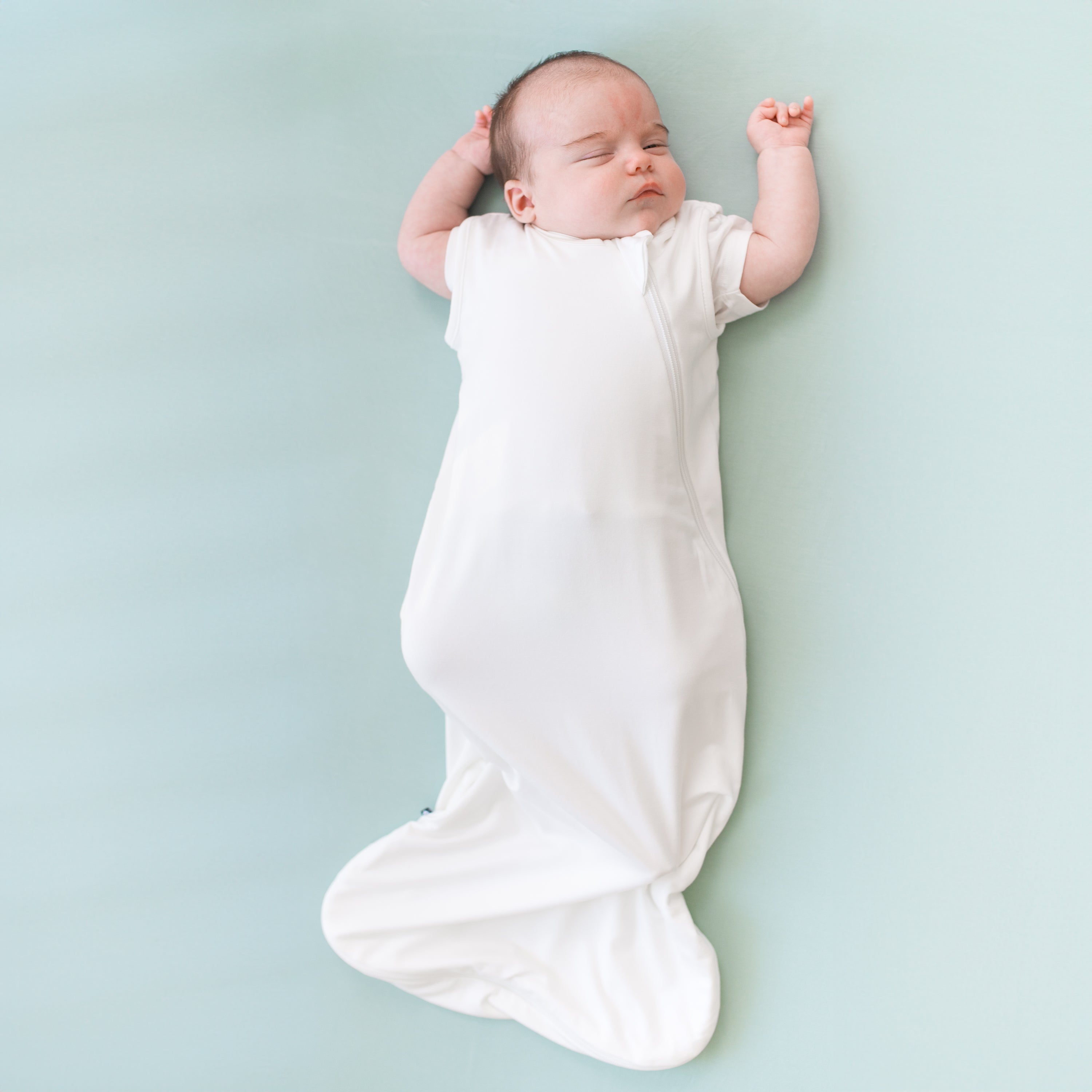 Baby laying down on a crib sheet in sage wearing a 0.5 tog sleep bag in cloud