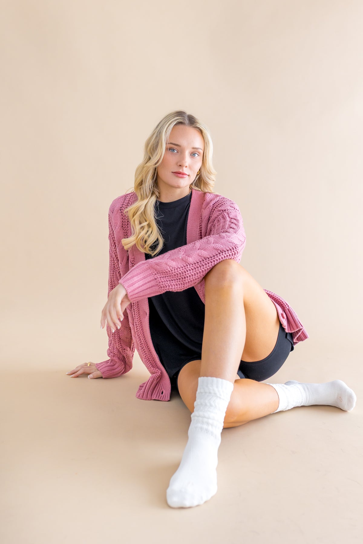 Female model sitting on the floor wearing the Adult Scrunch Socks in Cloud with a black shirt and black shorts underneath a pink sweater
