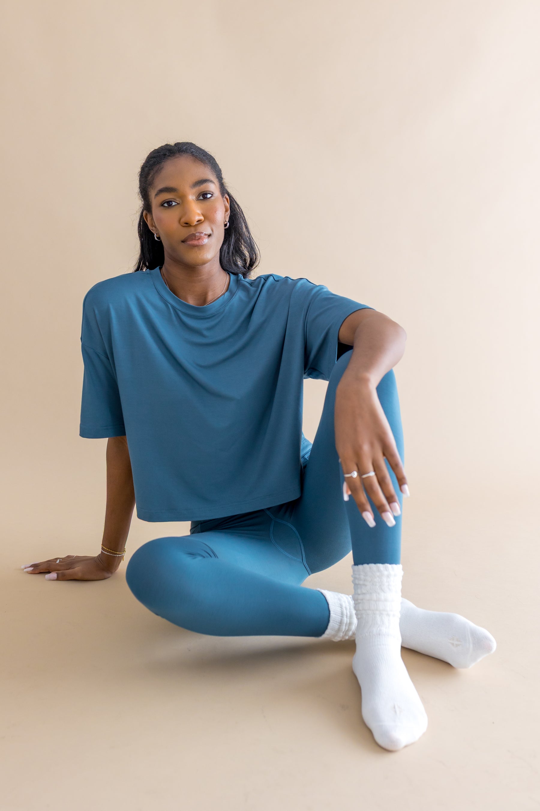 Female model sitting on the floor wearing the Adult Scrunch Socks in Cloud with blue leggings and blue shirt