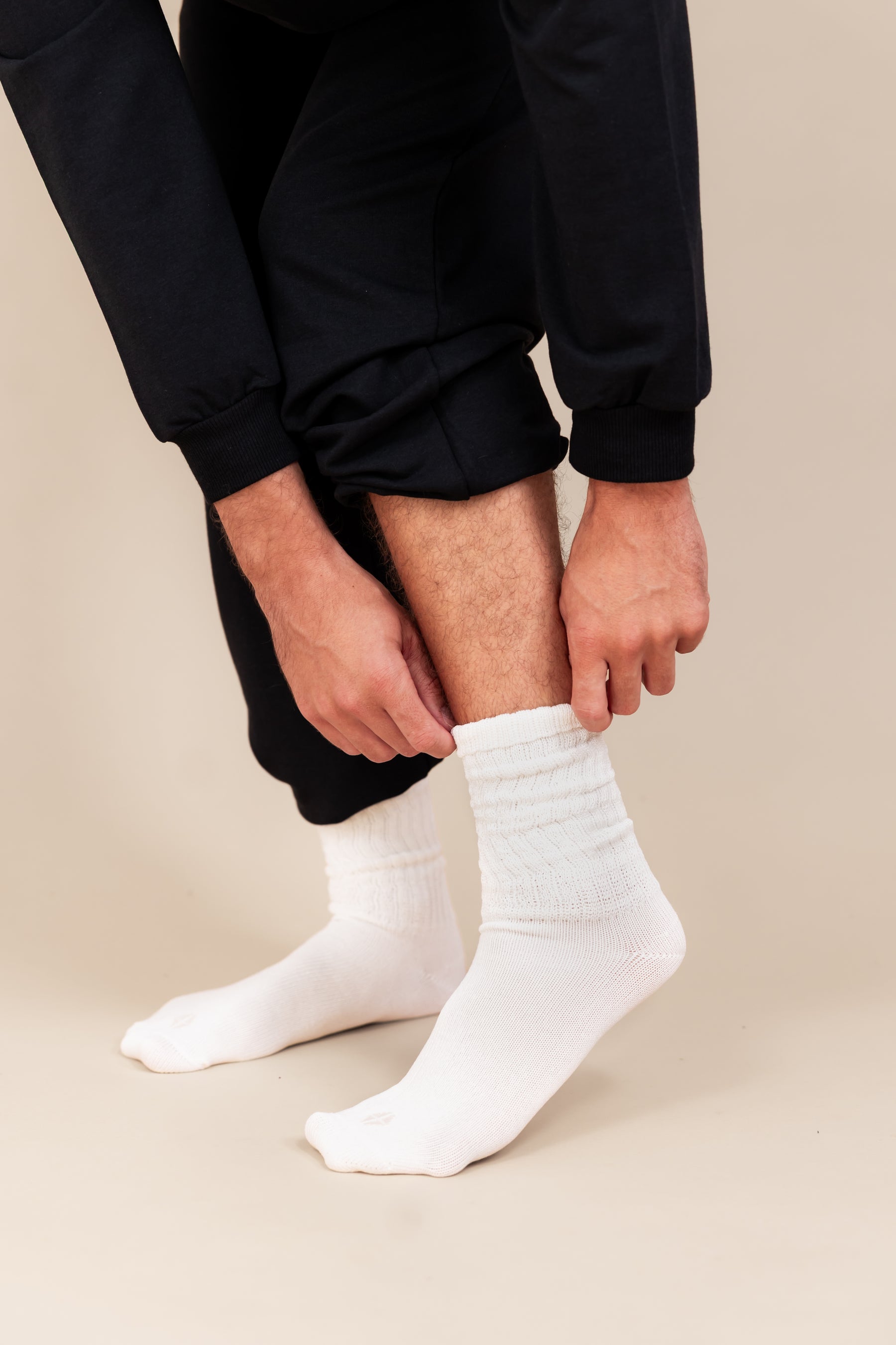 Modal pulling up Adult Scrunch Socks in Cloud color on his feet with black jogger set on a beige background