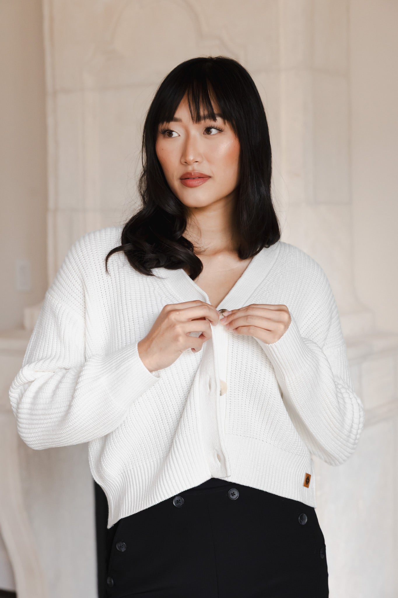 Modal buttoning the Chunky Knit Women's Cropped Cardigan in Cloud over a black outfit