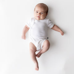Infant laying on a white surface wearing the Pointelle Kimono Bodysuit in Cloud