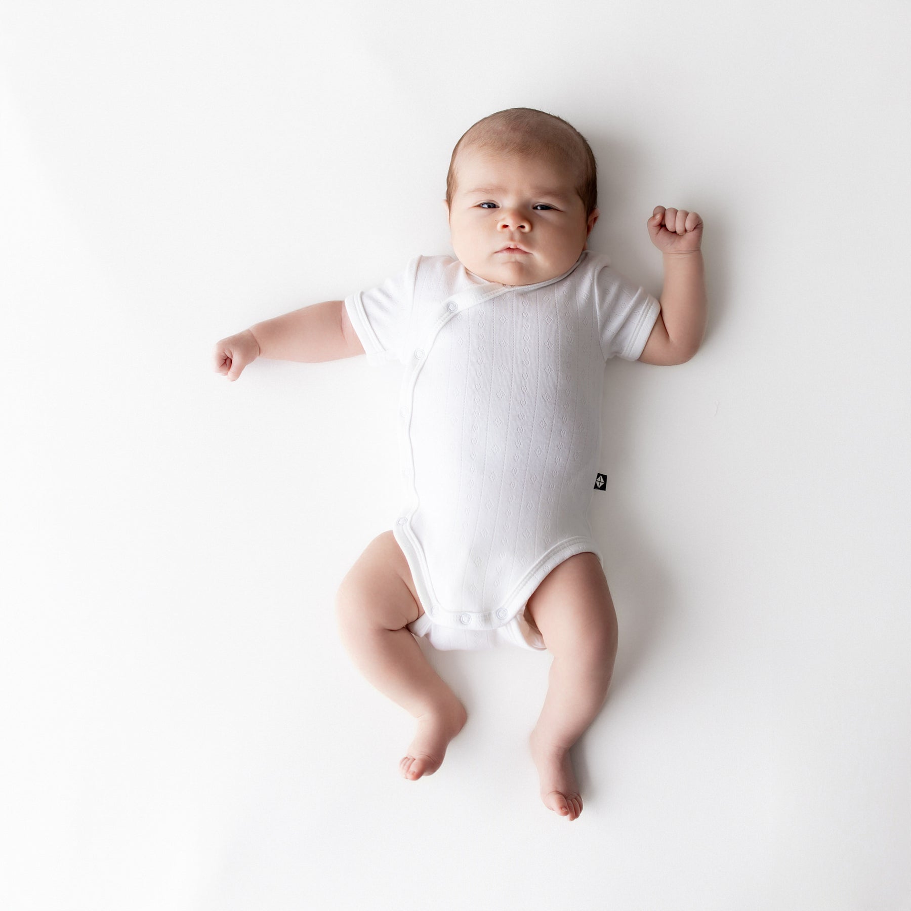 Newborn wearing the Pointelle Kimono Bodysuit in Cloud laying on a white surface