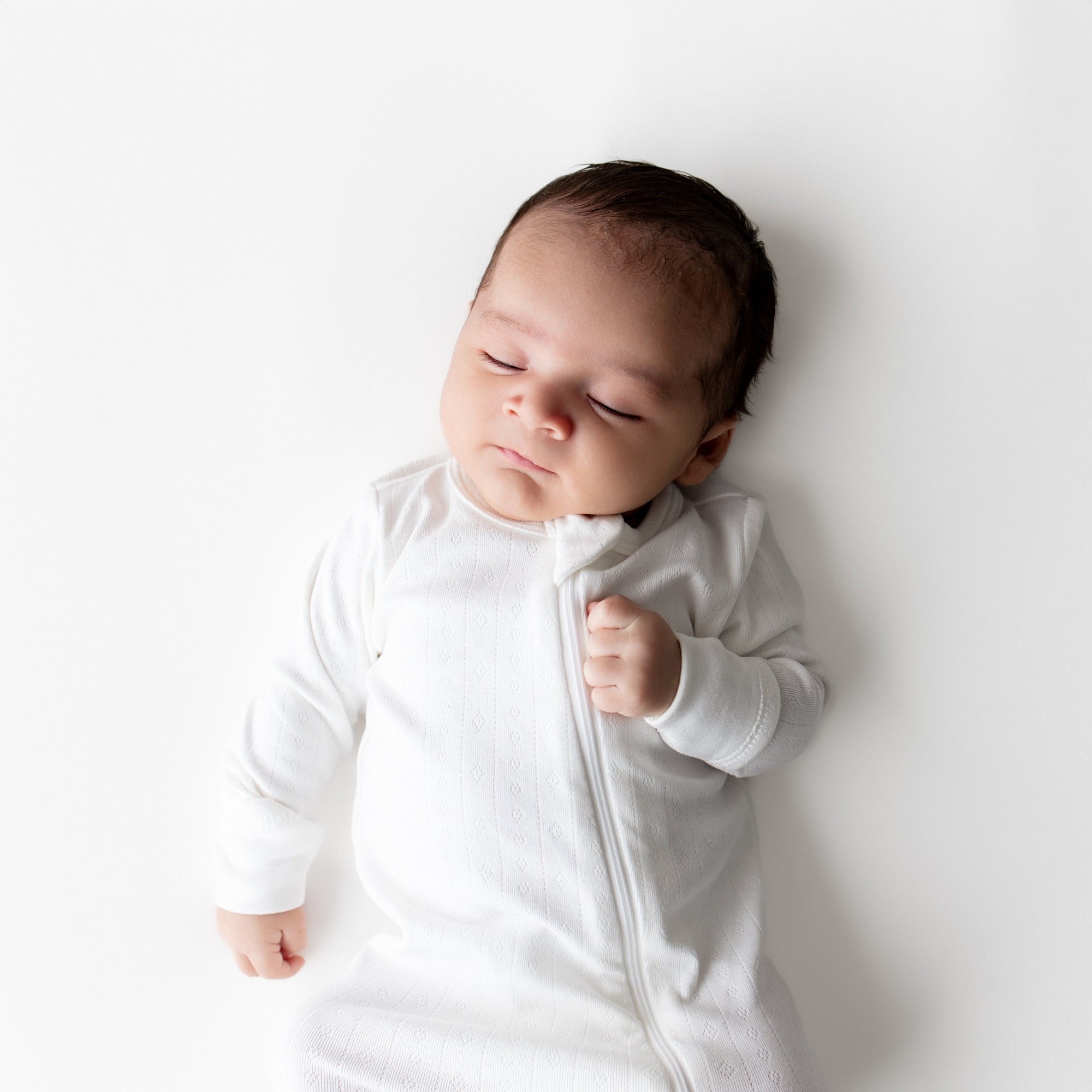 Close up a sleeping newborn wearing the Pointelle Zippered Footie in Cloud