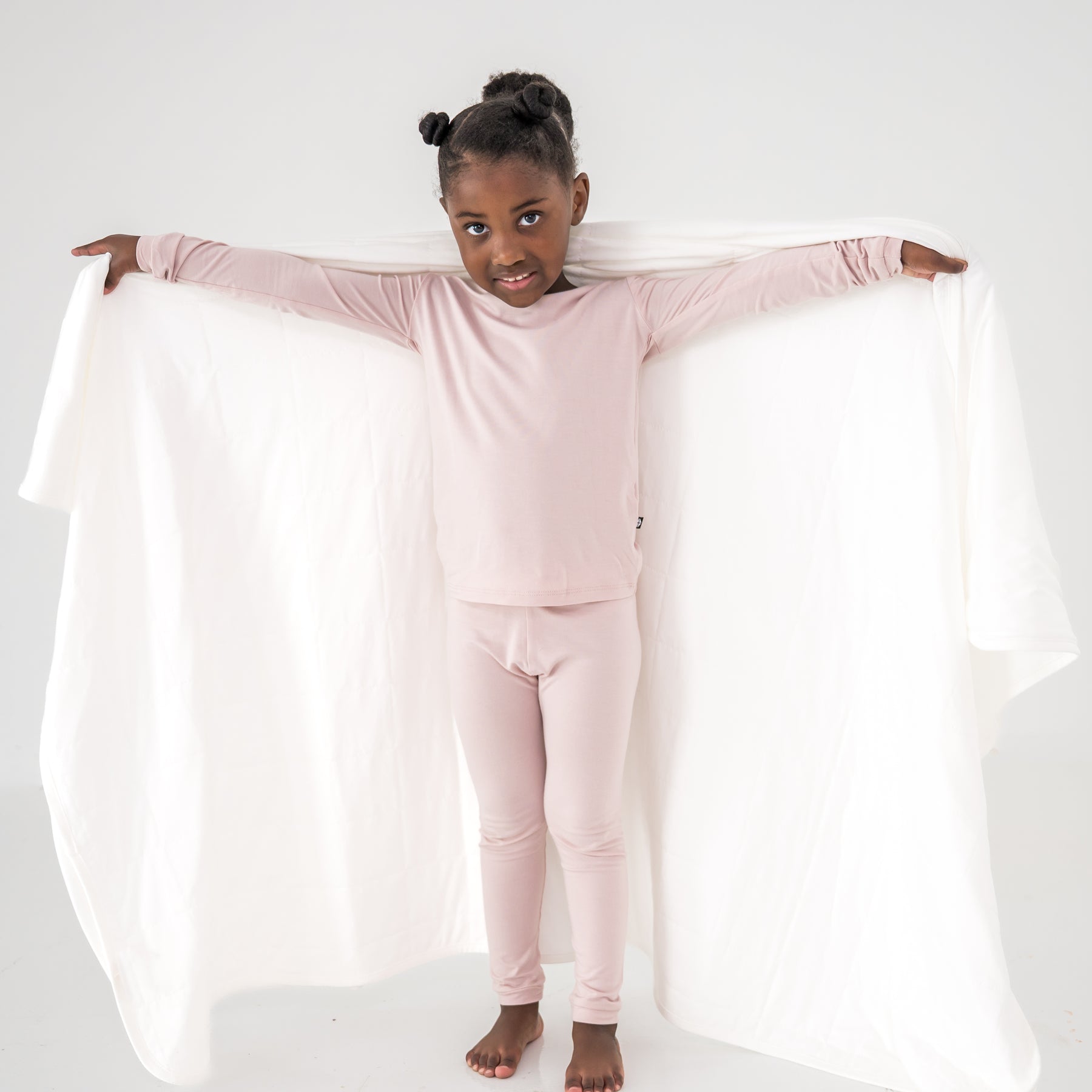 Child wearing pink pajamas holding a white blanket against a white background