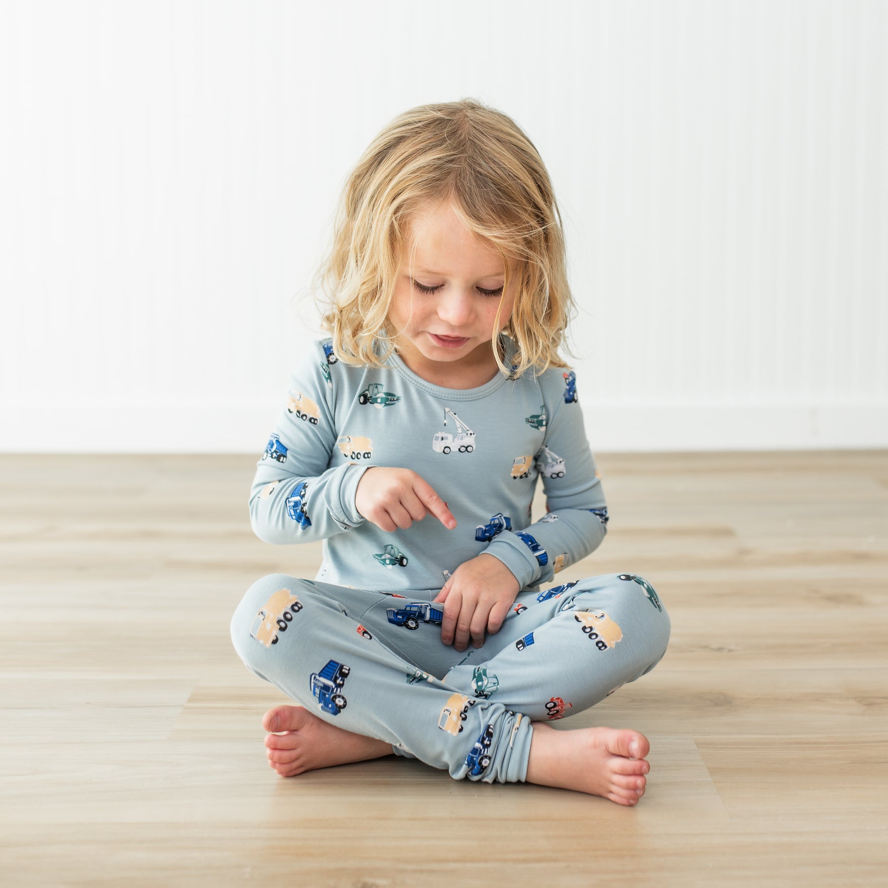 Child wearing a blue pajama set with vehicle patterns on a wooden floor.