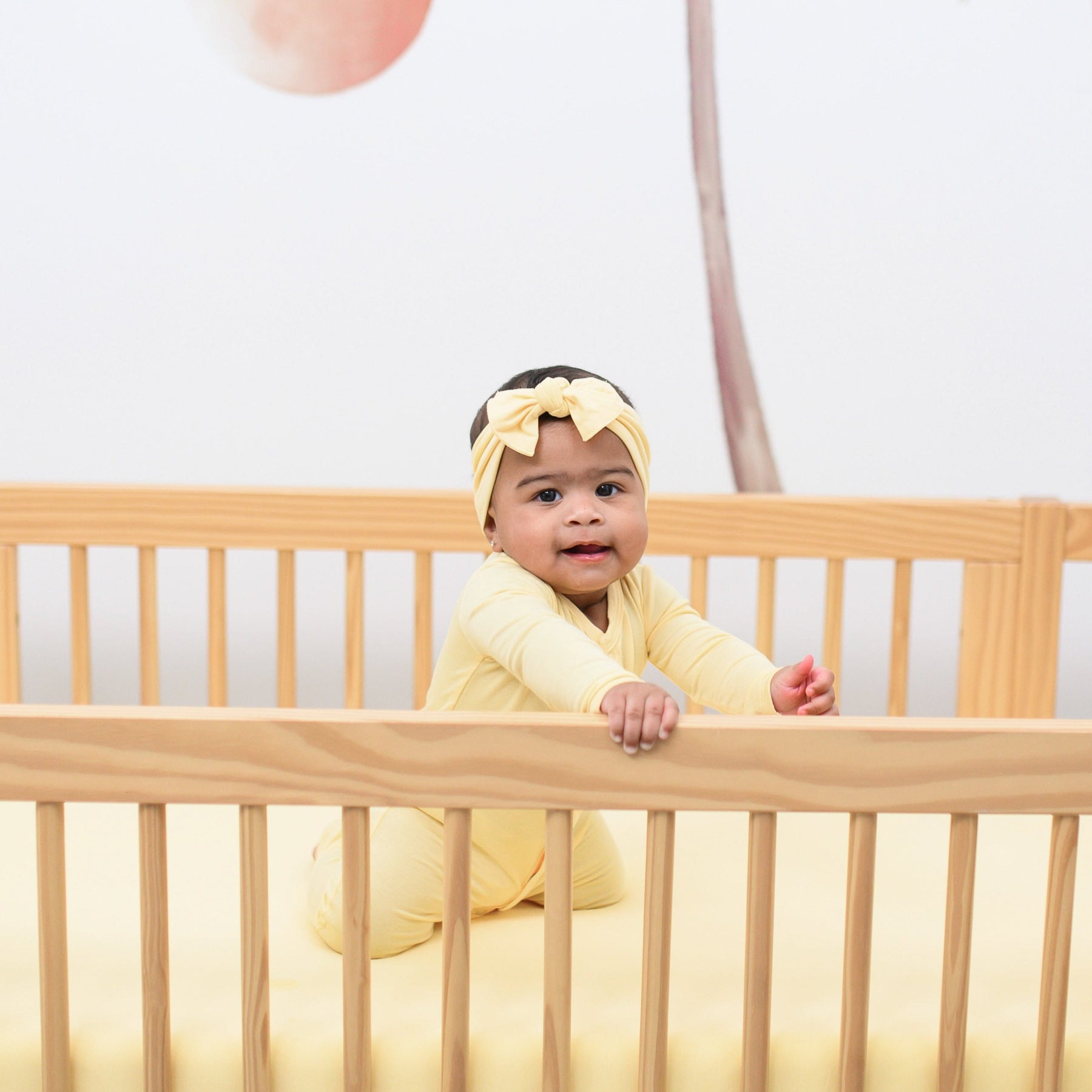 baby sitting in a crib wearing snap romper and bow in lilikoi 