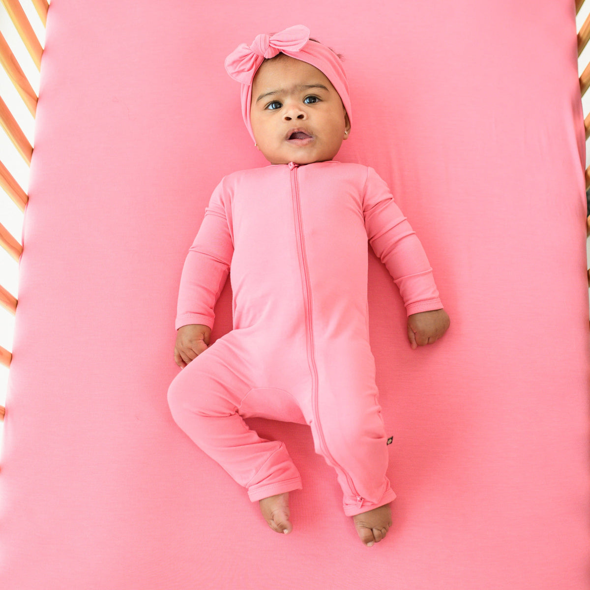 baby in zippered romper and bow in color guava 