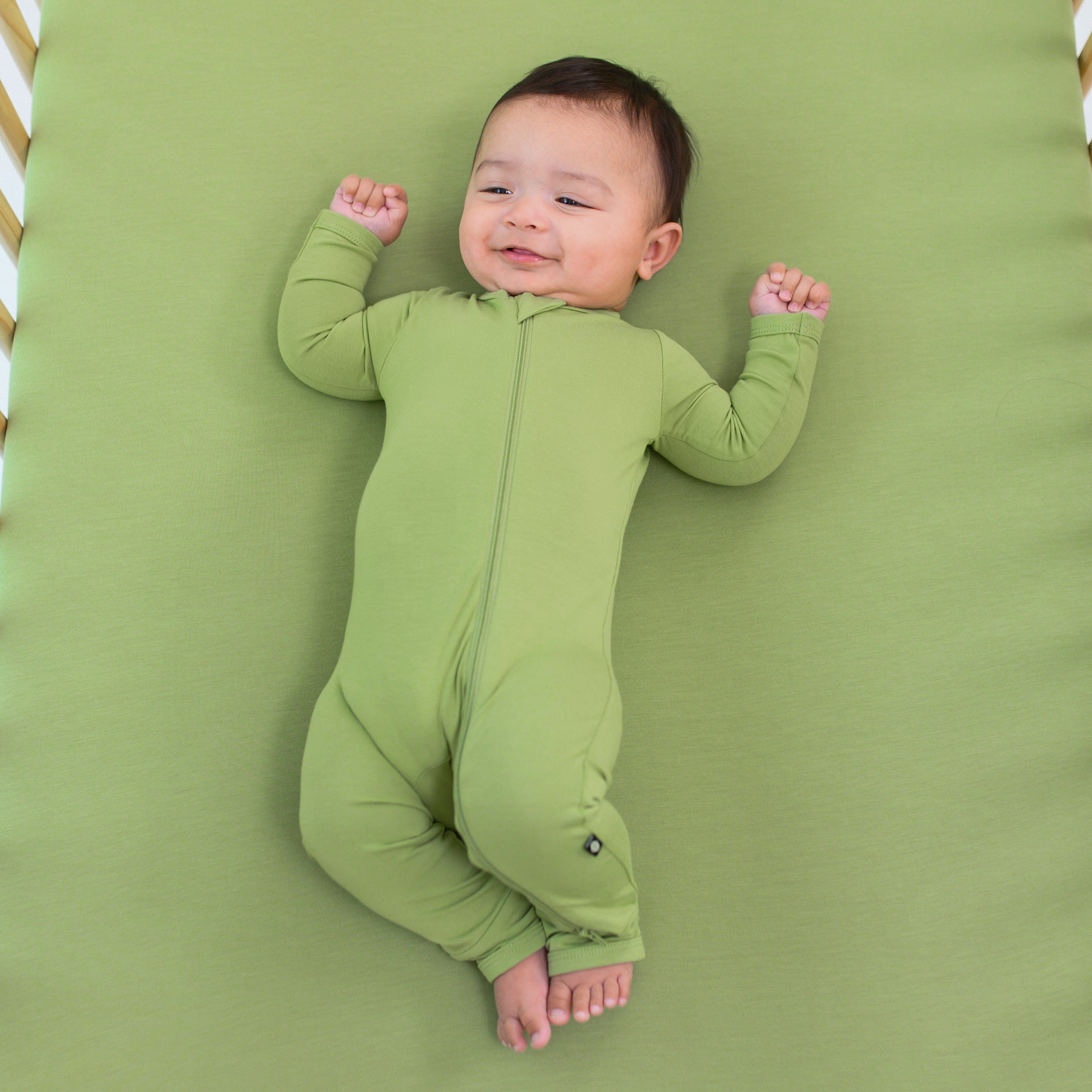 baby laying on a crib with honu crib sheet while wearing zippered romper in honu