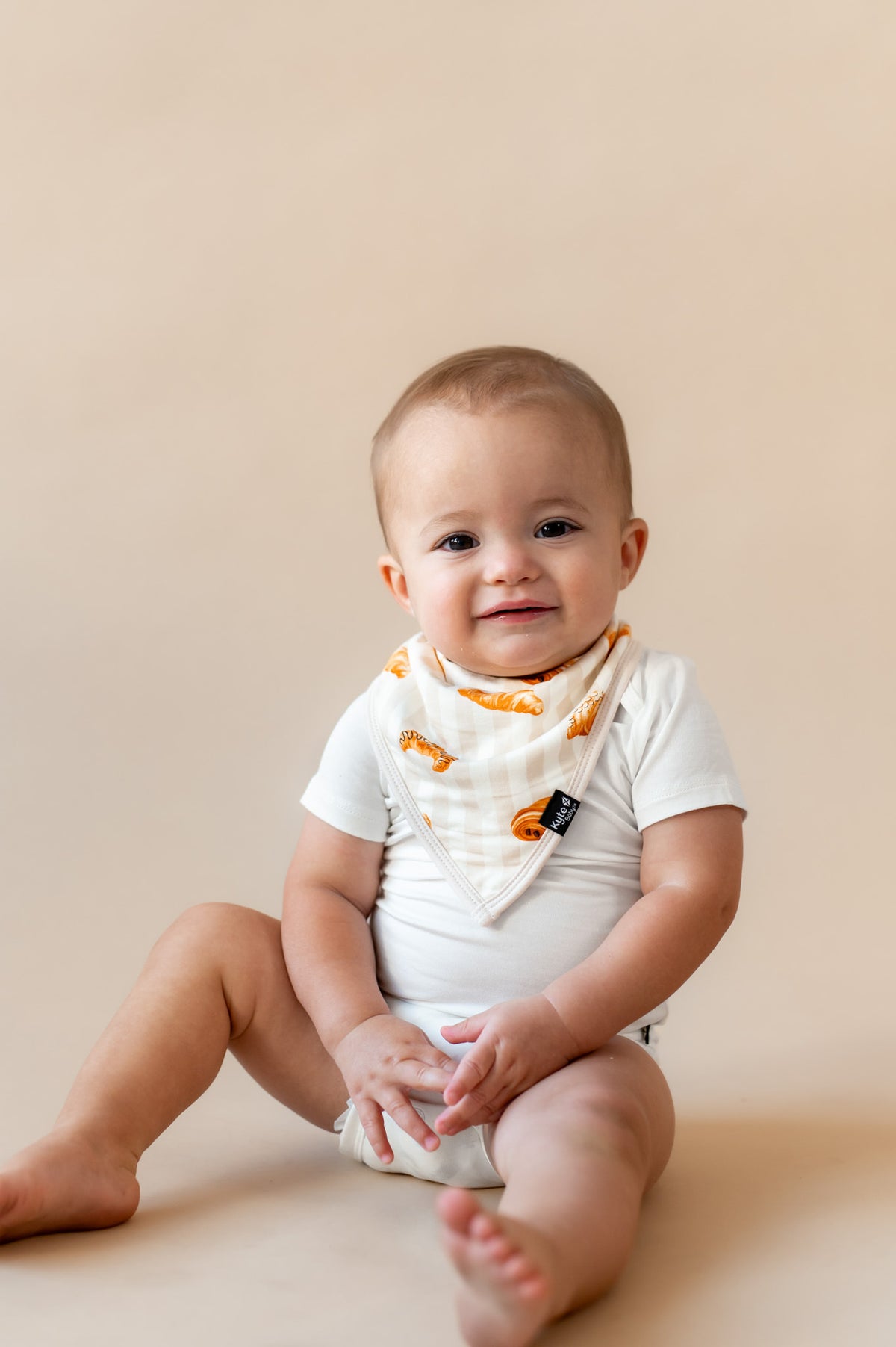 Baby wearing Bib with Croissant print over white bodysuit on a beige background