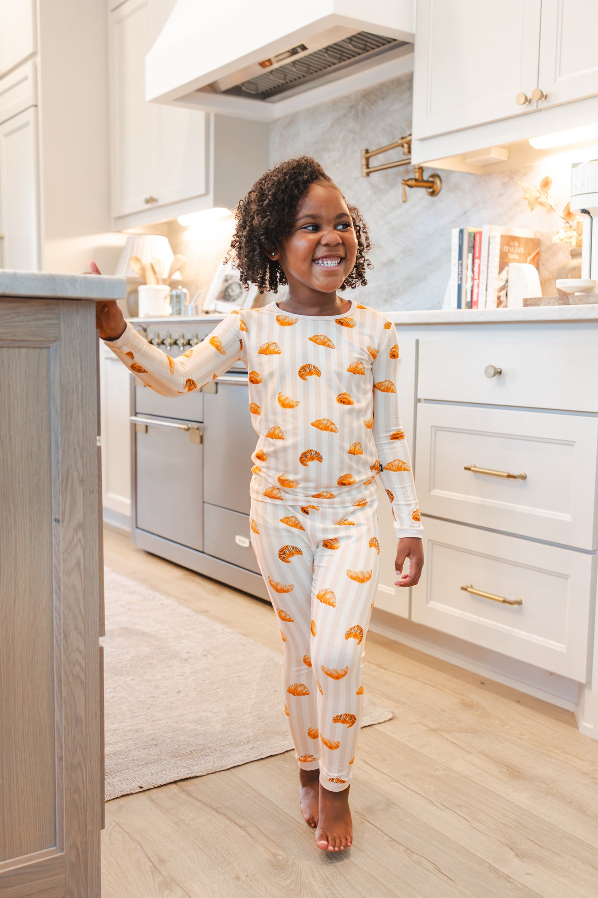 Girl standing in kitchen wearing Long Sleeve Pajamas with Croissant print 