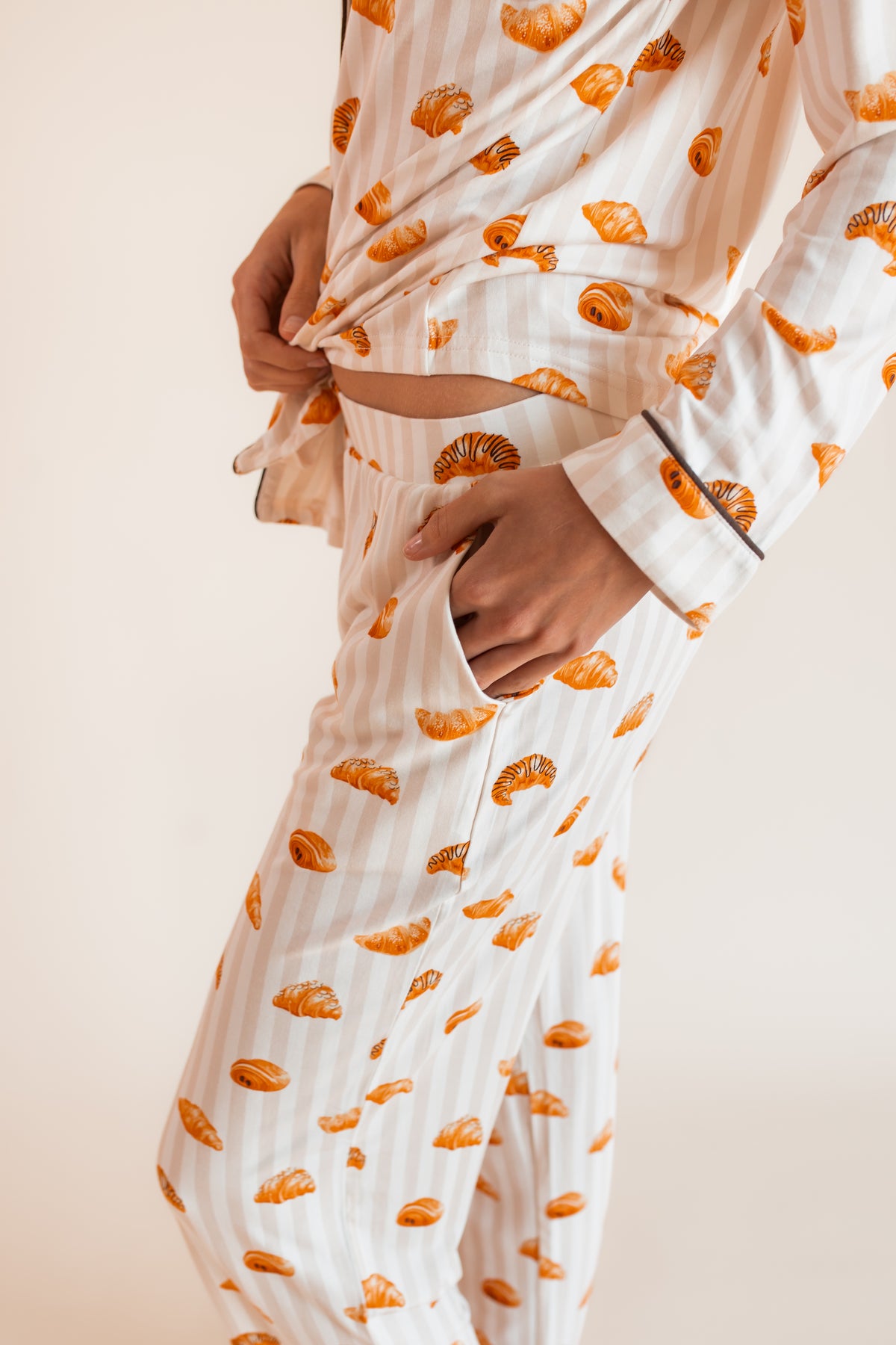 Model showcasing the pocket on Long-Sleeved Women's Pajama Set in Croissant print on a beige background