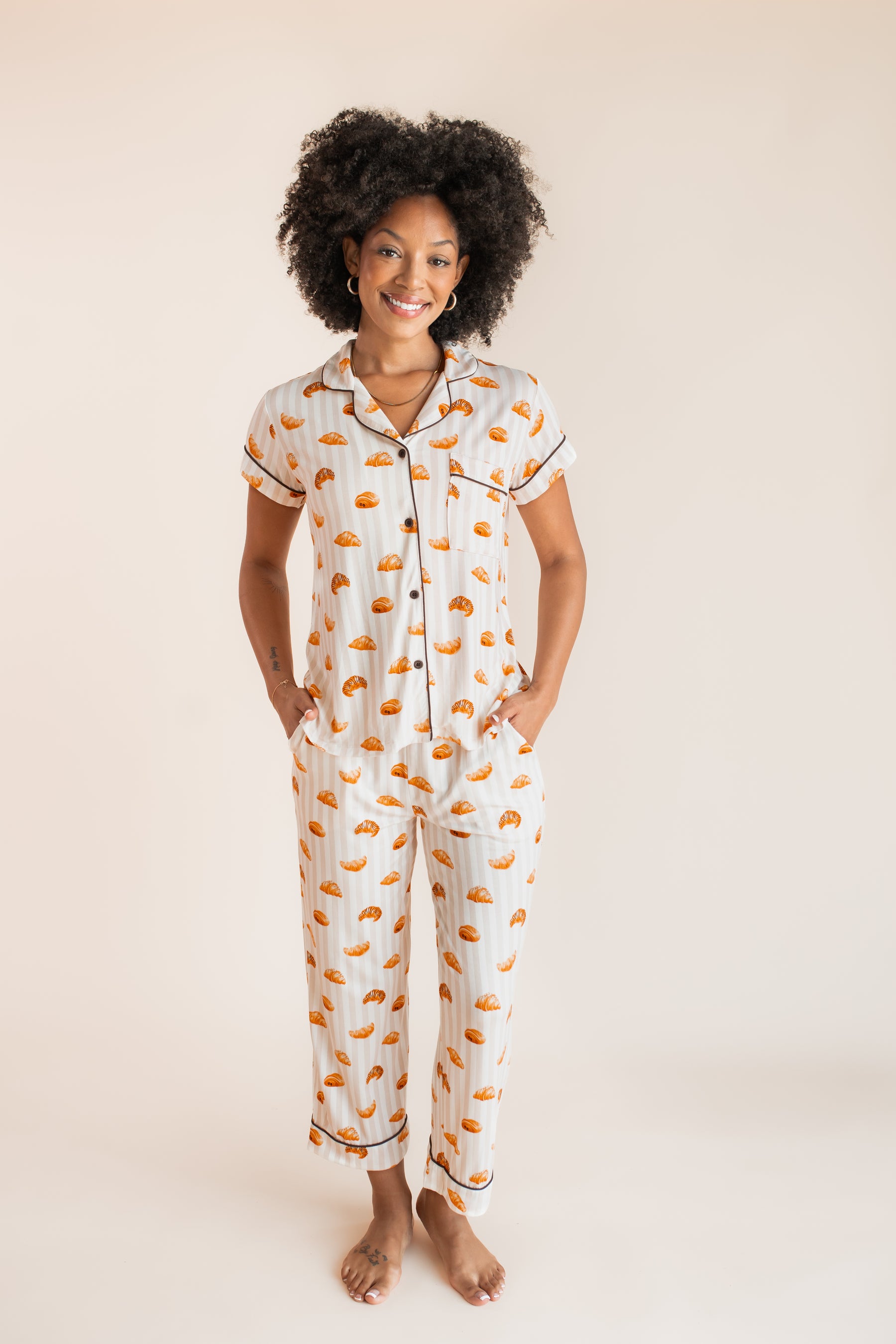 Model smiling in Women's Short Sleeve Cropped Pajama Set with Croissant print with pockets on a beige background