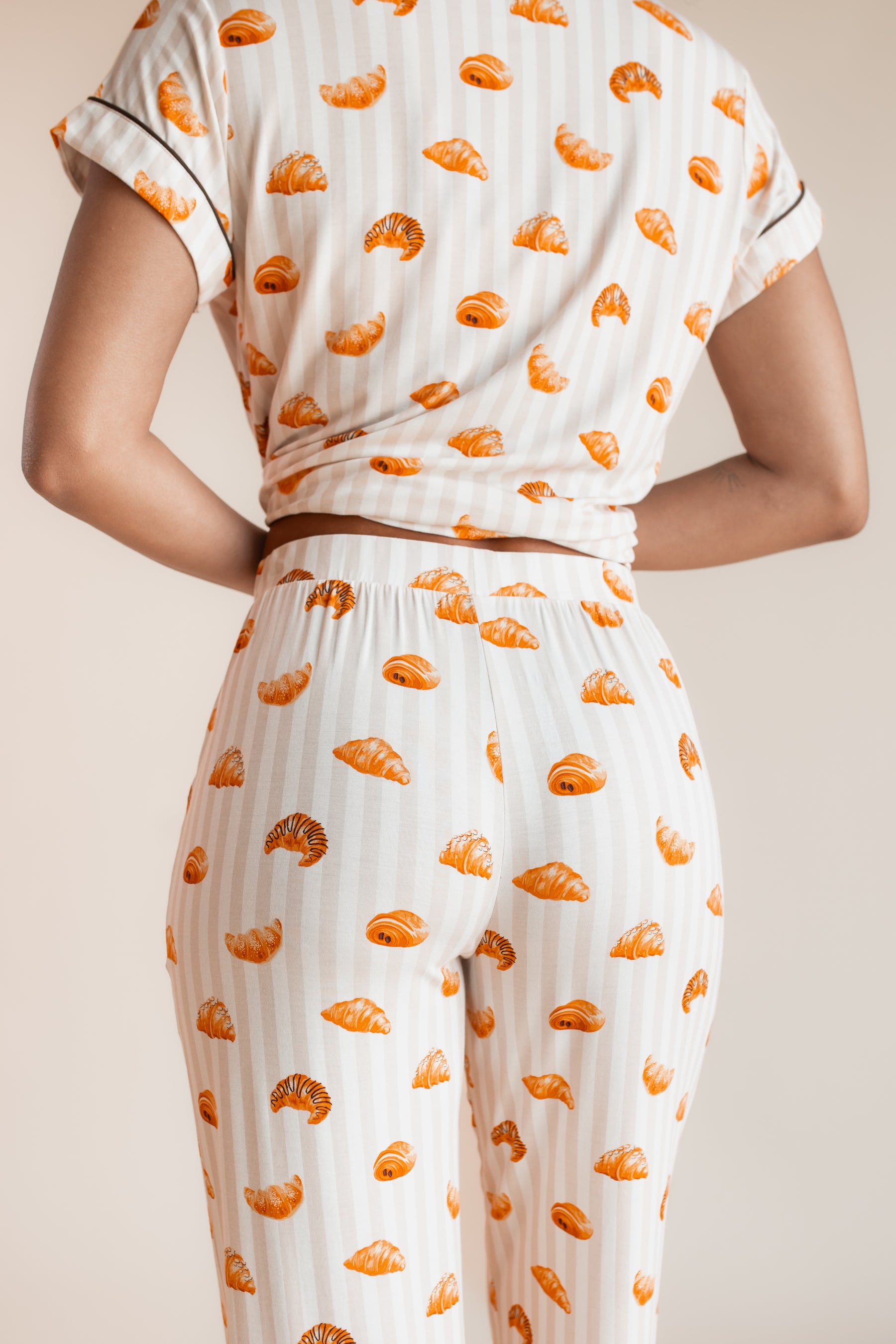 Back side of Model wearing Women's Short Sleeve Cropped Pajama Set with Croissant print on a beige background