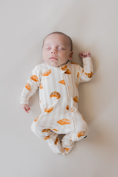Baby sleeping in Zippered Footie with Croissant print on a beige background
