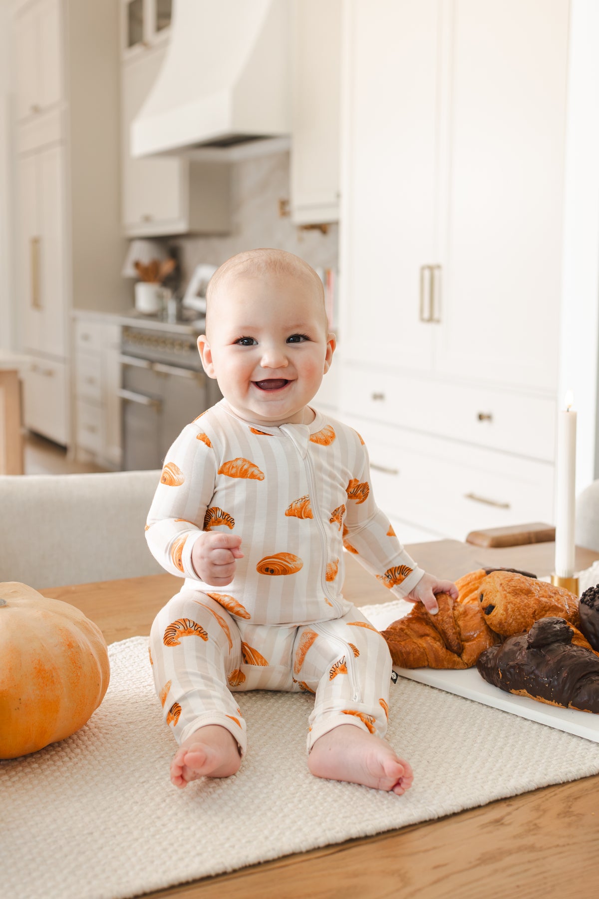 Baby sitting on a table wearing Zippered Romper with Croissant print