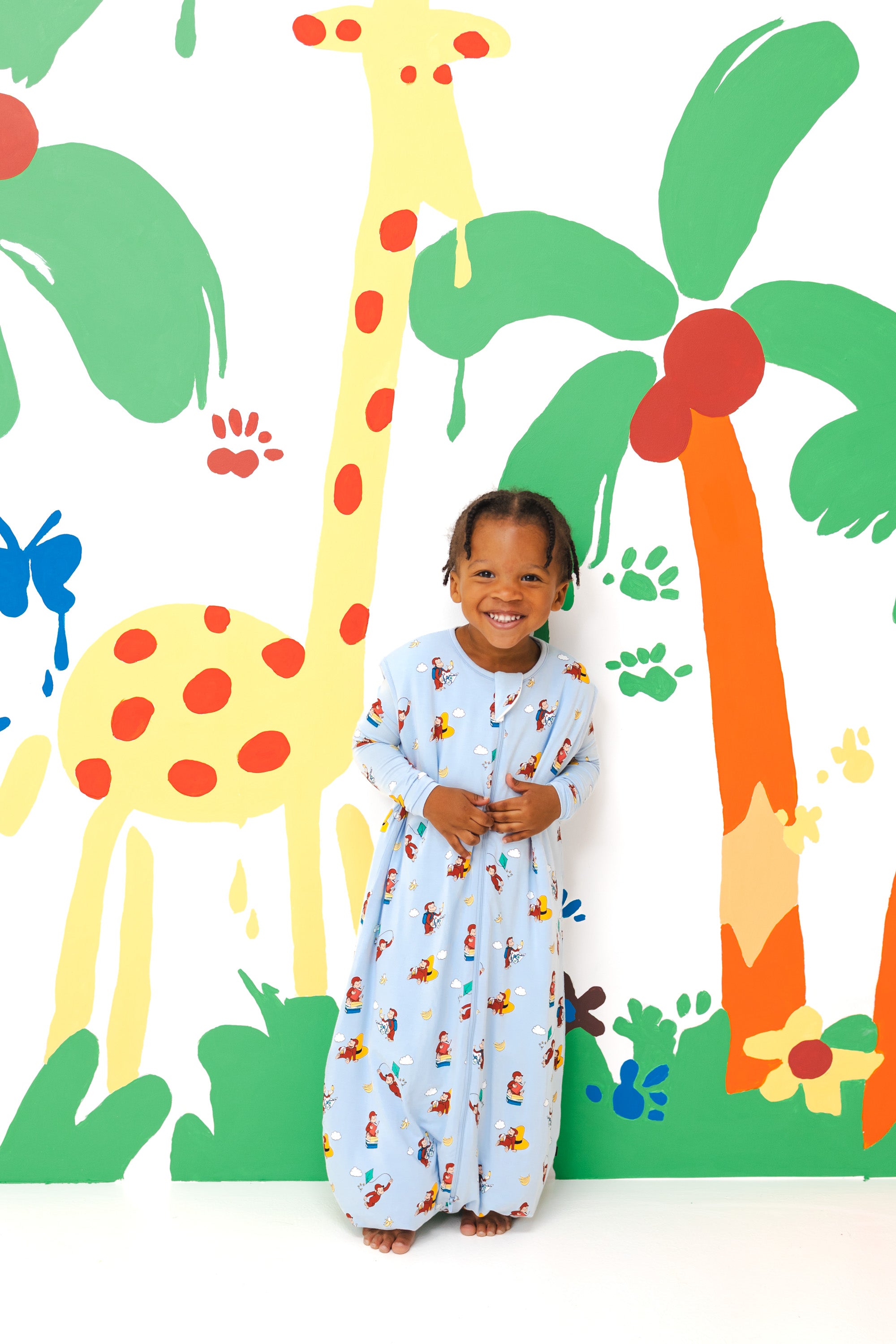 Girl wearing Sleep Bag Walker in Curious George 1.0 print standing in front of a colorful background