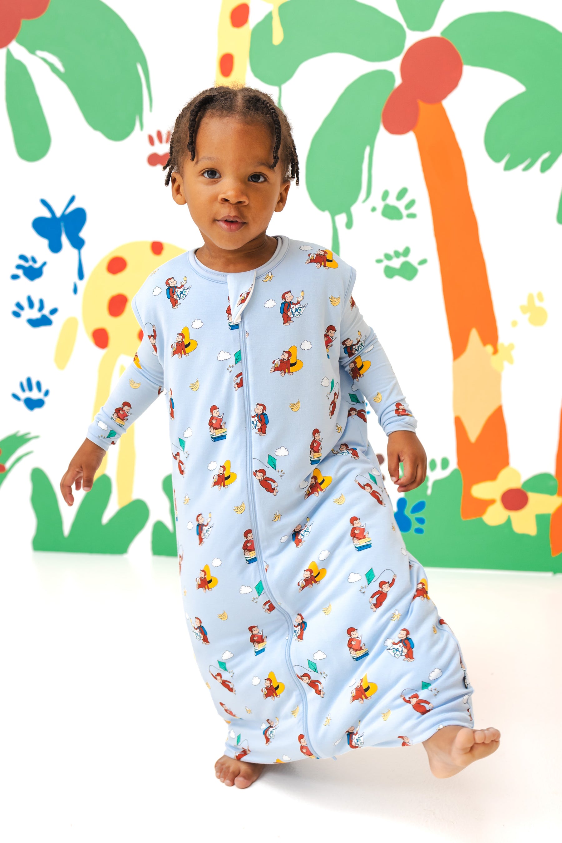 Girl posing in Sleep Bag Walker in Curious George 1.0 print standing in front of a colorful background