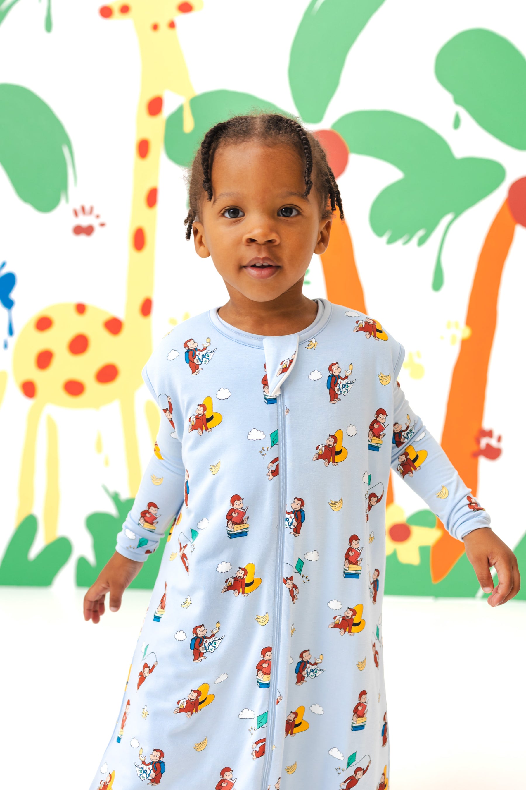 Girl wearing Sleep Bag Walker in Curious George 1.0 print standing in front of a colorful background