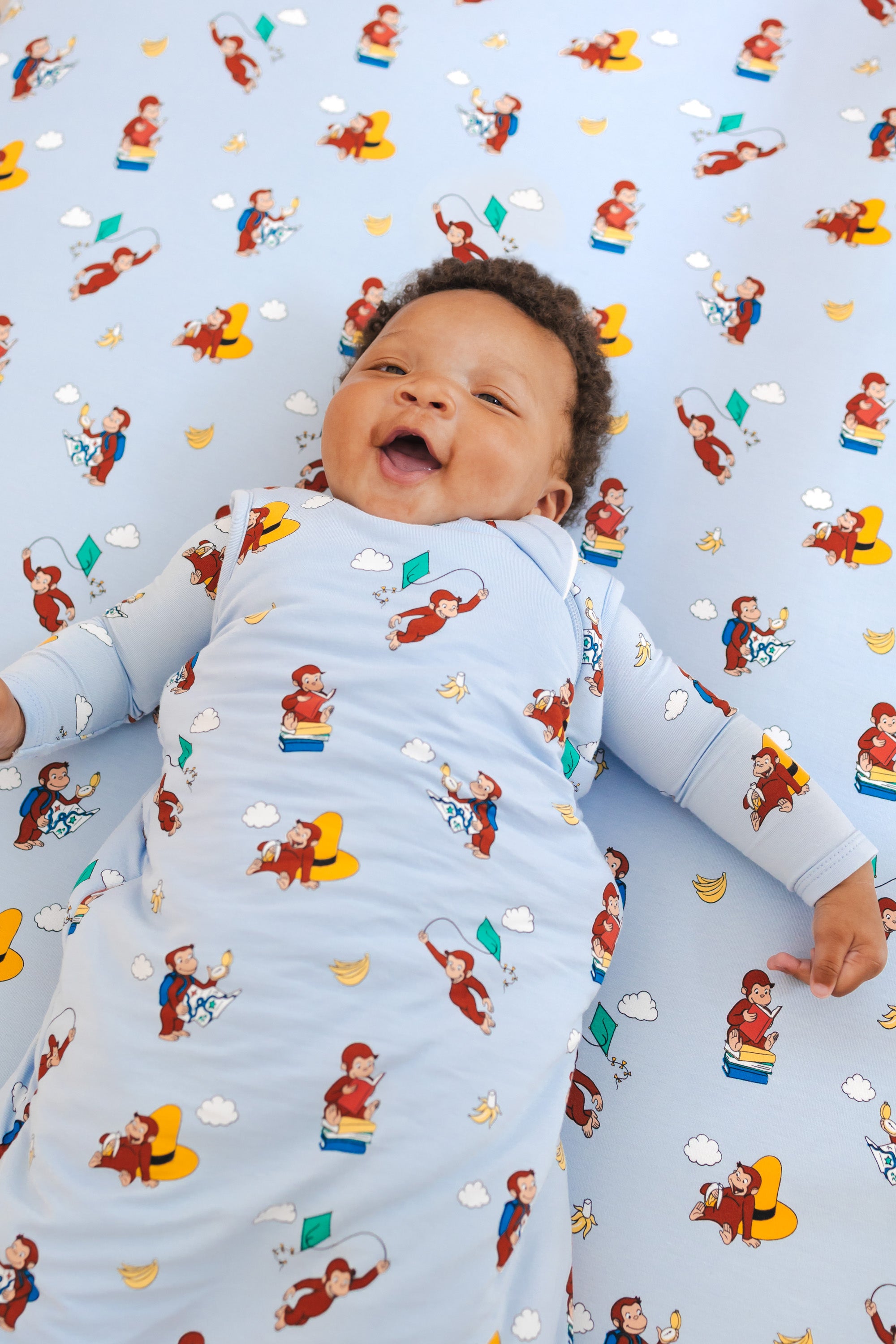 Baby in Sleep Bag in Curious George 1.0 print lying on a similar print crib sheet