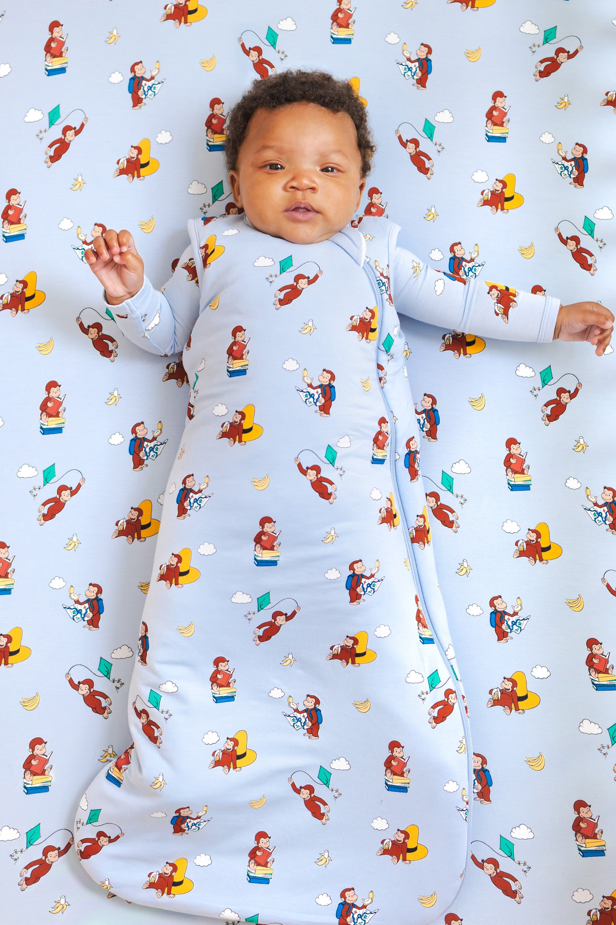 Baby lying in Sleep Bag in Curious George 1.0 print over a similar print crib sheet