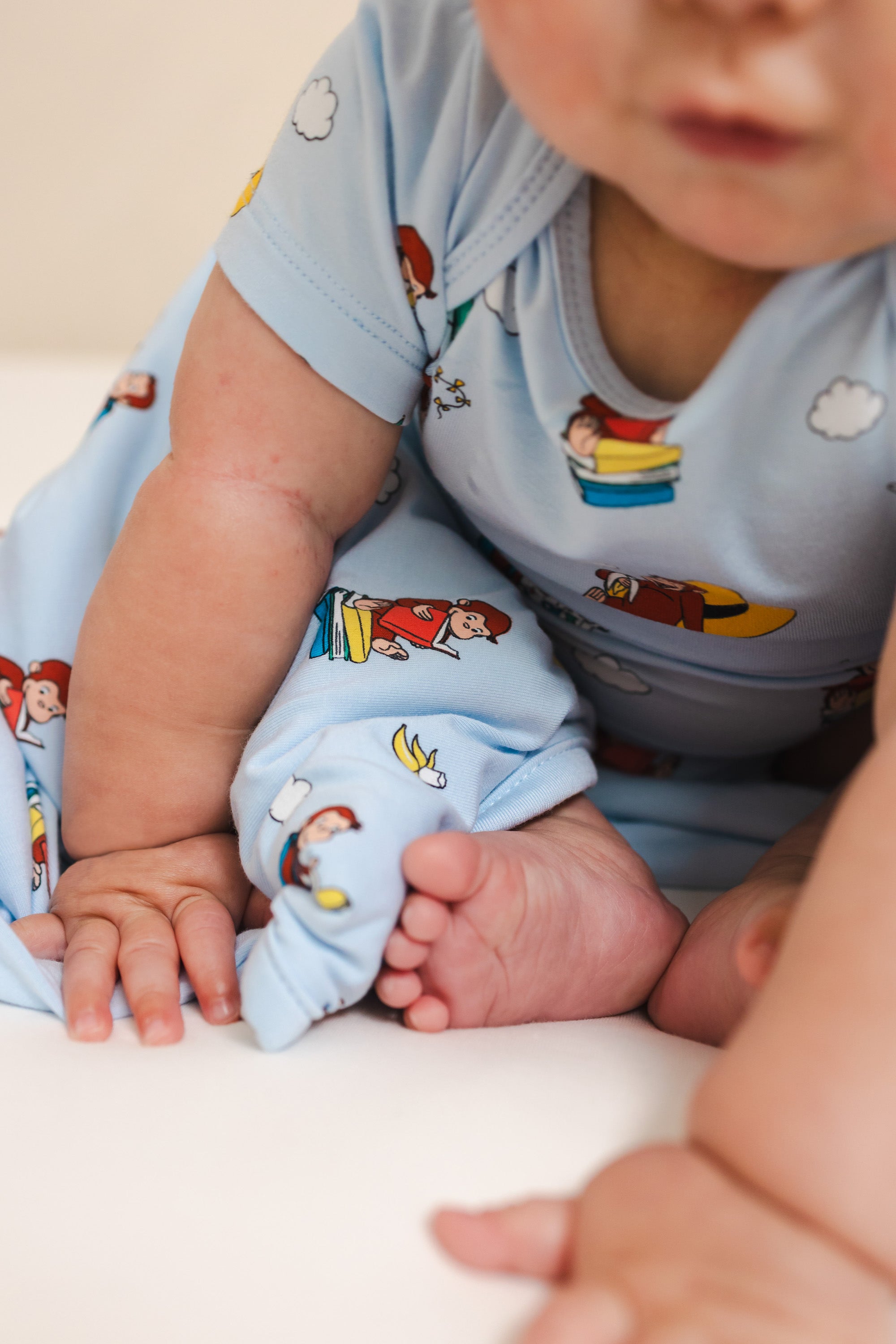 Baby with Curious George 1.0 print Baby blanket wearing similar print bodysuit on a beige background