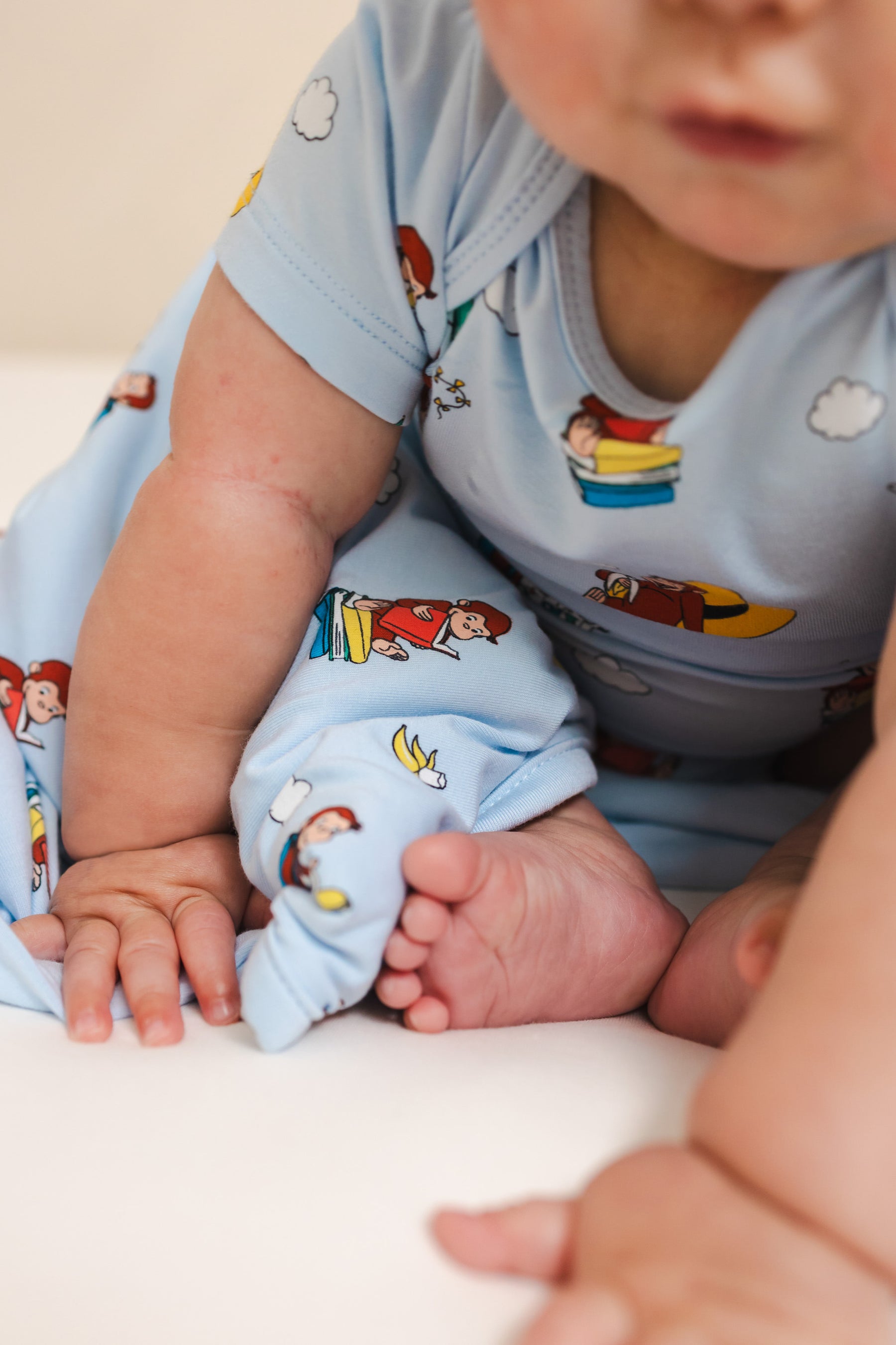 Baby with Curious George 1.0 print Baby blanket wearing similar print bodysuit on a beige background