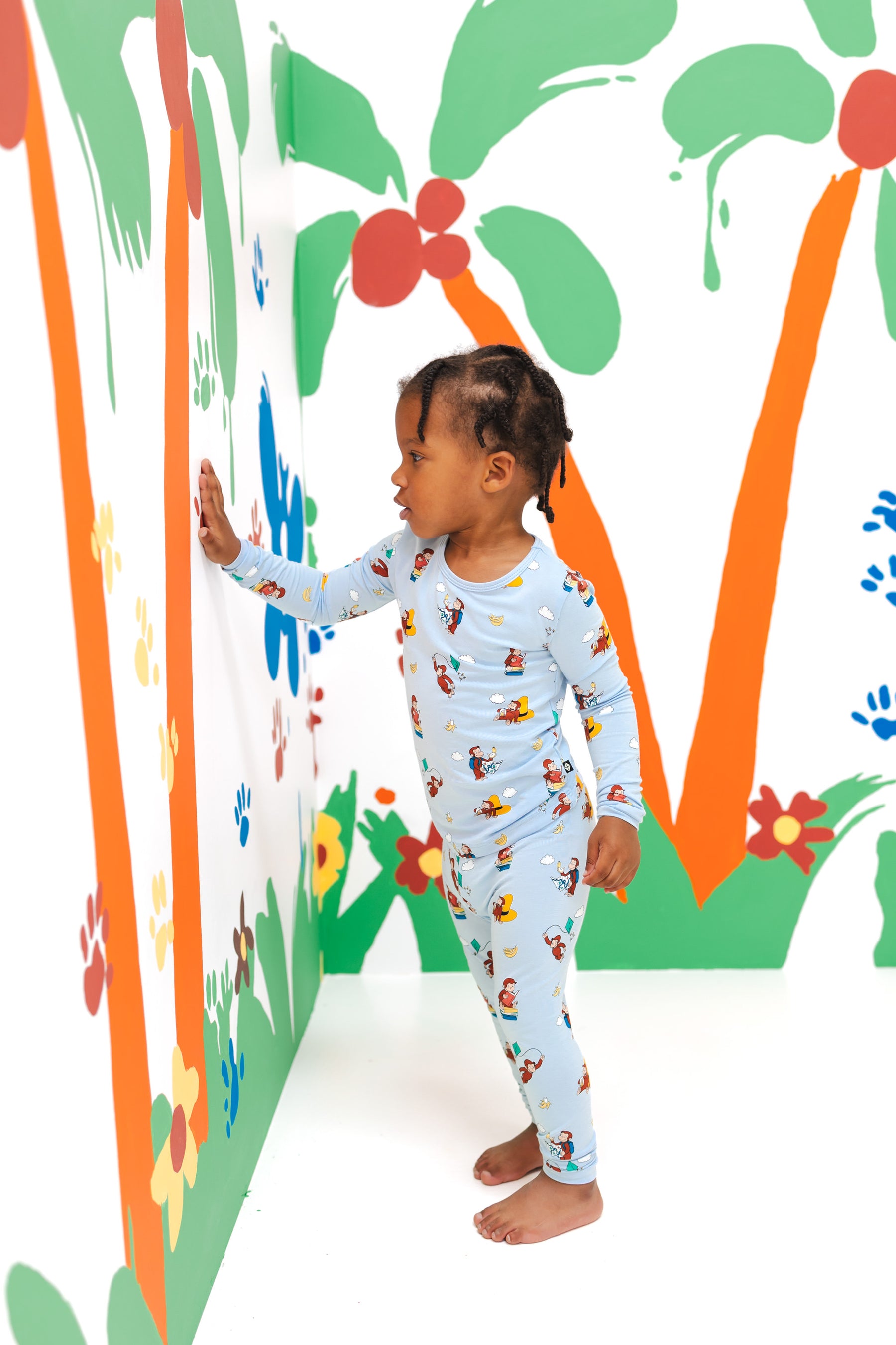 Girl wearing Long Sleeve Pajamas in Curious George print standing in a colorful background