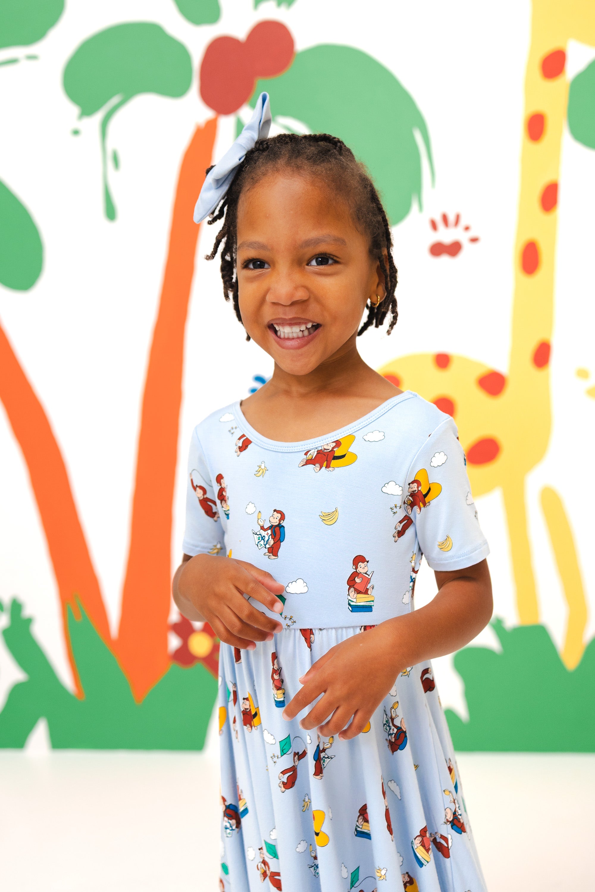Girl wearing Twirl Dress in Curious George print standing in front of a colorful background