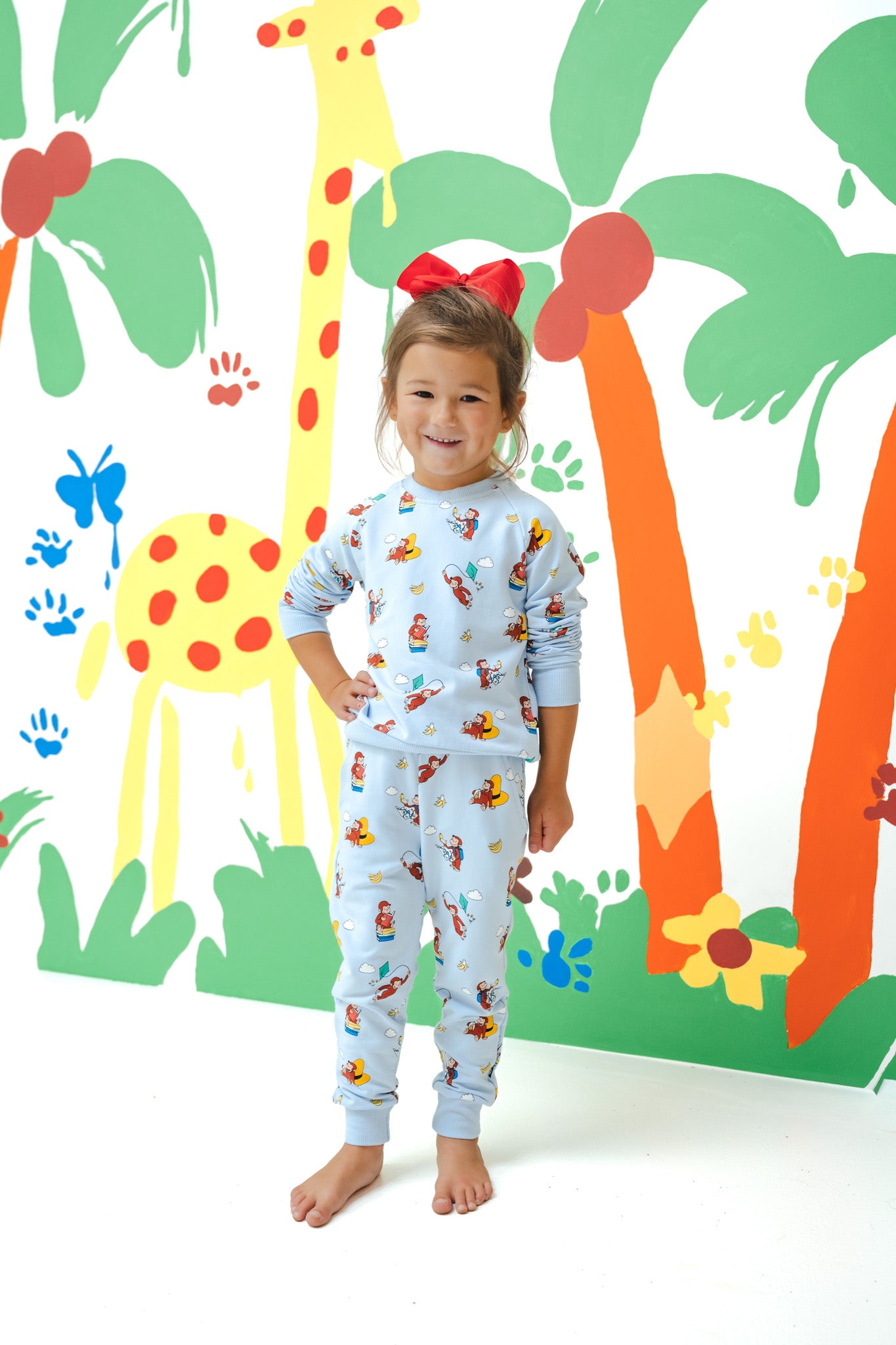 Girl posing in Long Sleeve Jogger Set in Curious George print standing in front of a colorful background