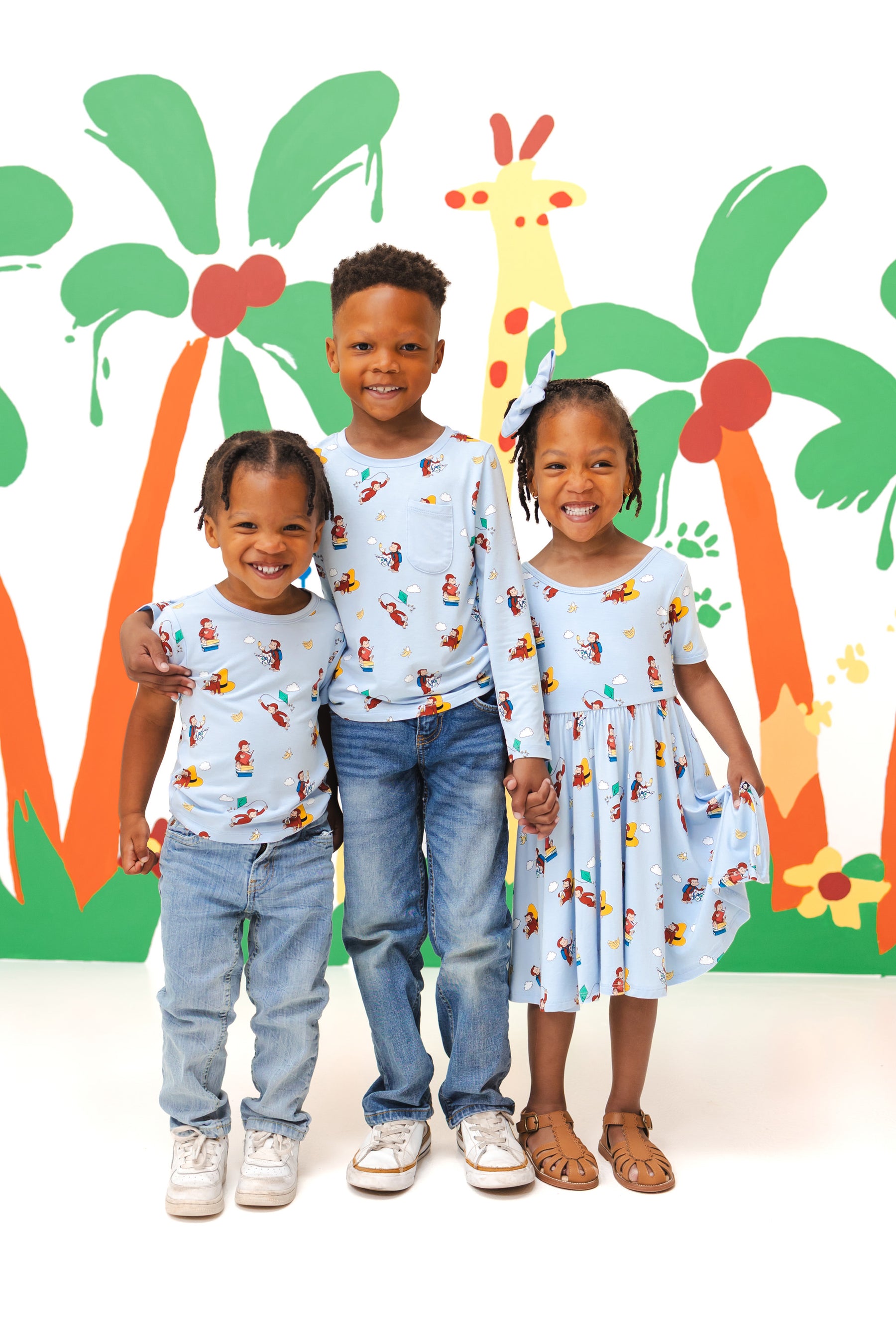 Kids standing in front of a colorful background wearing Long Sleeve Toddler Crew Neck Tee, Twirl dress and Toddler basic tee in Curious George print