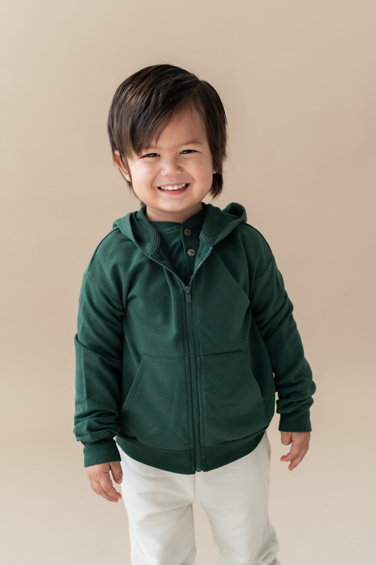 child modeling a dark green zip up hoodie and cream pants 