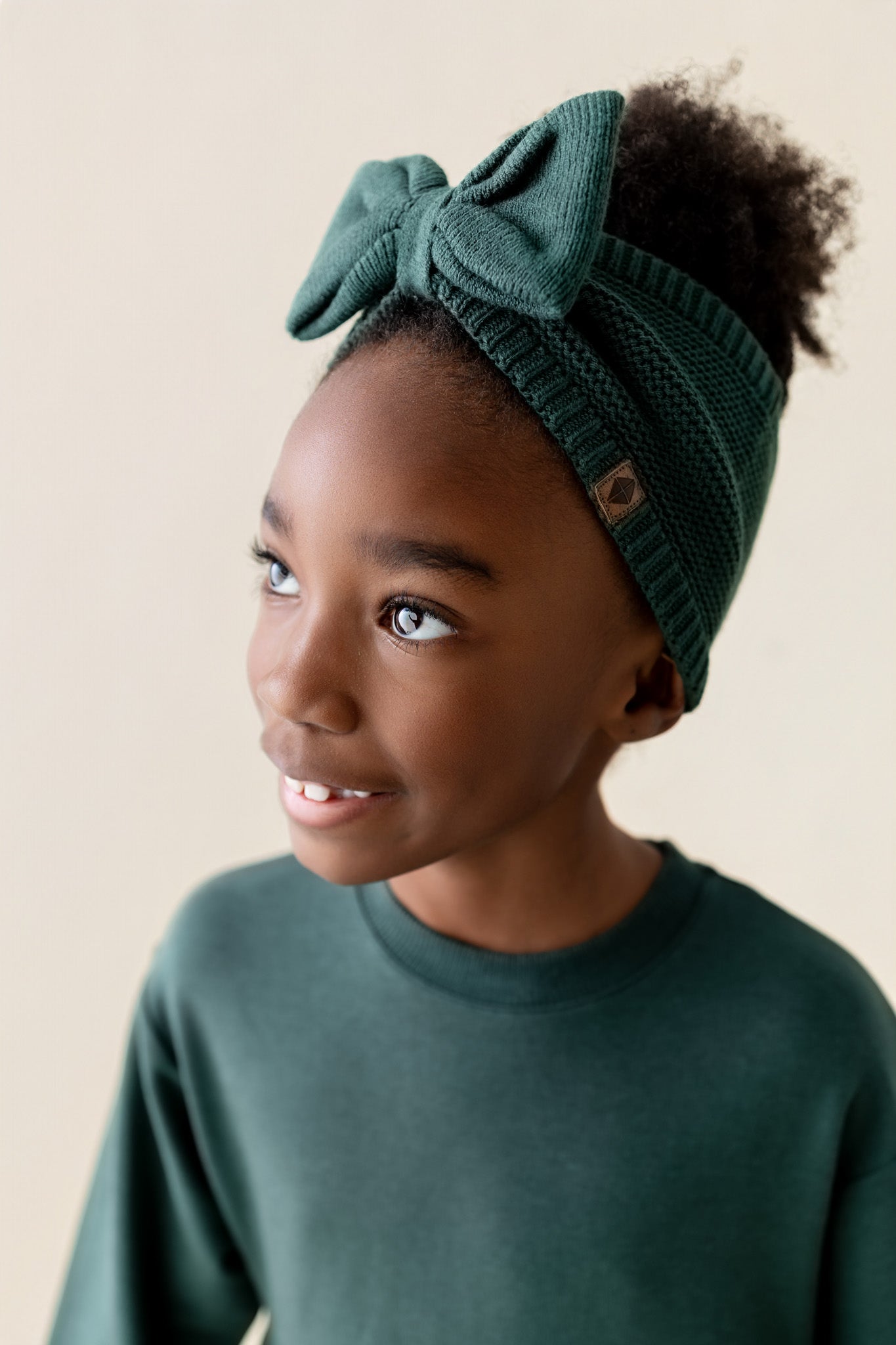 Girl wearing Long Sleeve Skater Dress in Cypress color with Chunky knit knotted bow headband on a beige background