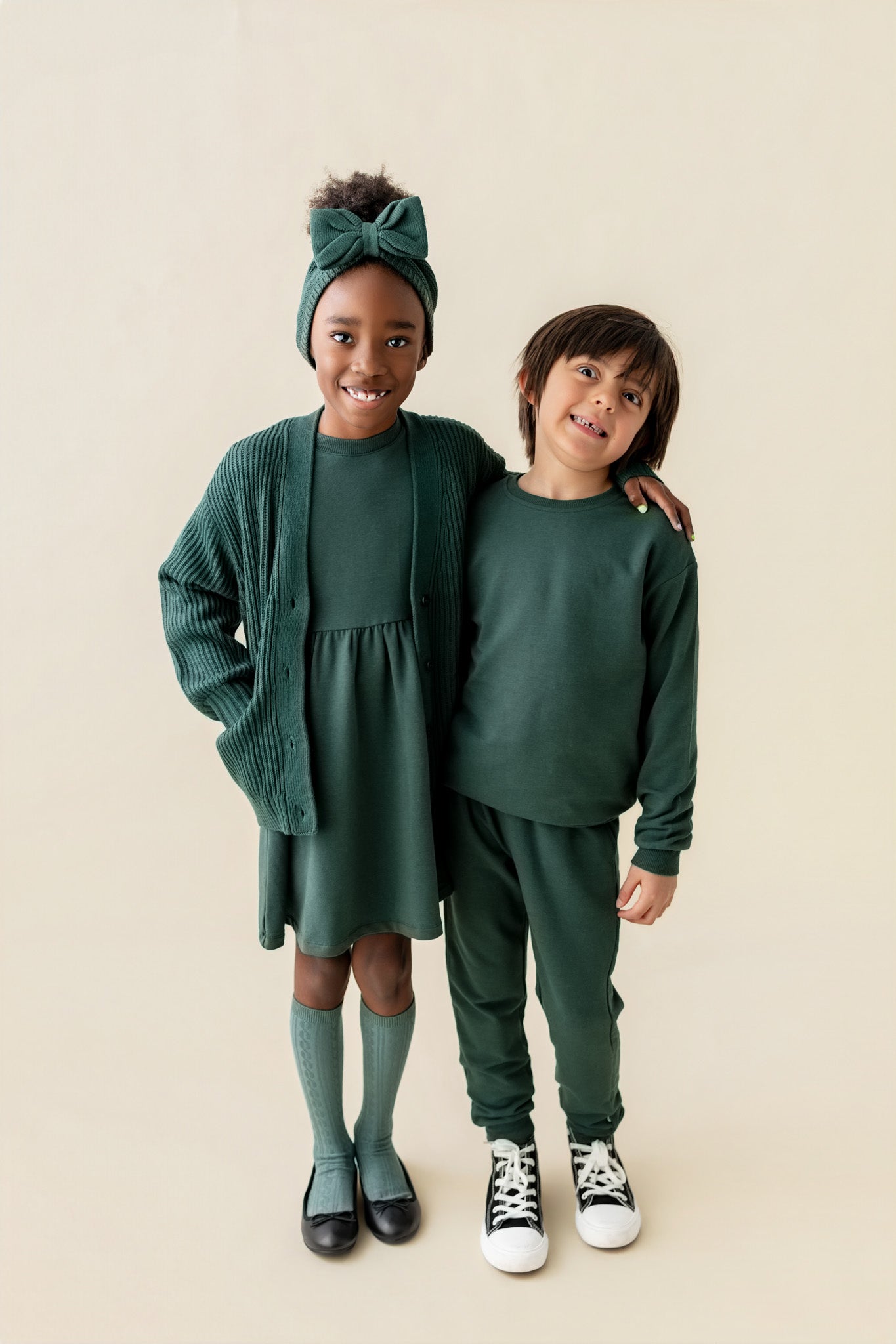 A boy wearing Long Sleeve Jogger Set in Cypress color and girl wearing Long sleeve skater dress in cypress color on a beige background