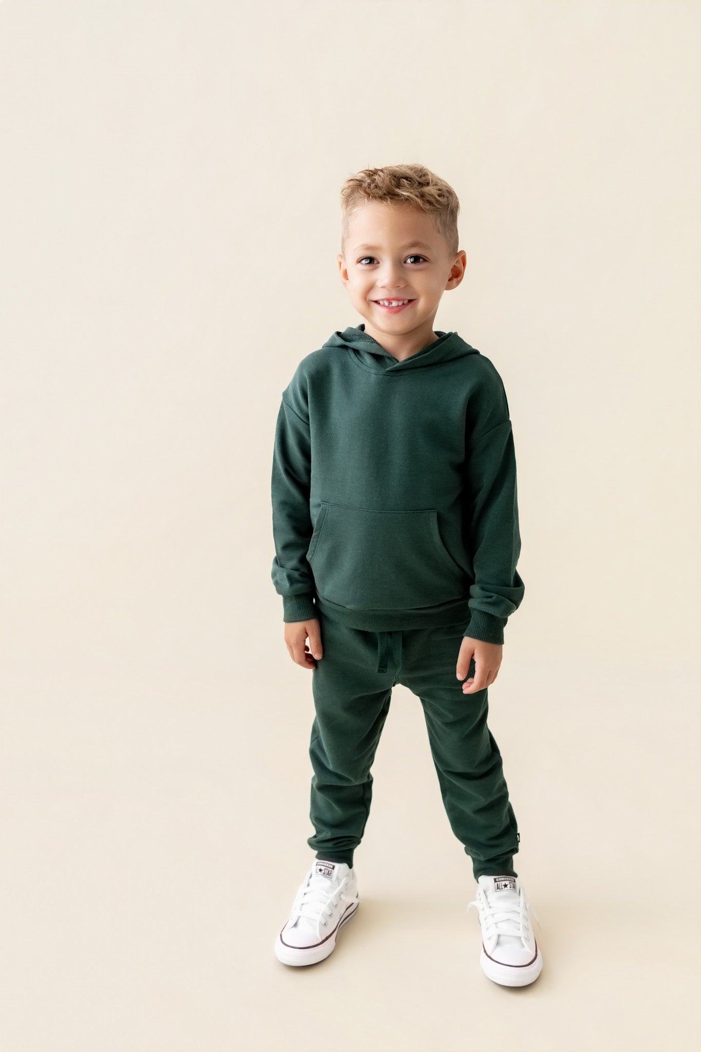 Boy wearing Hoodie in Cypress color over similar color jogger pants on a beige background