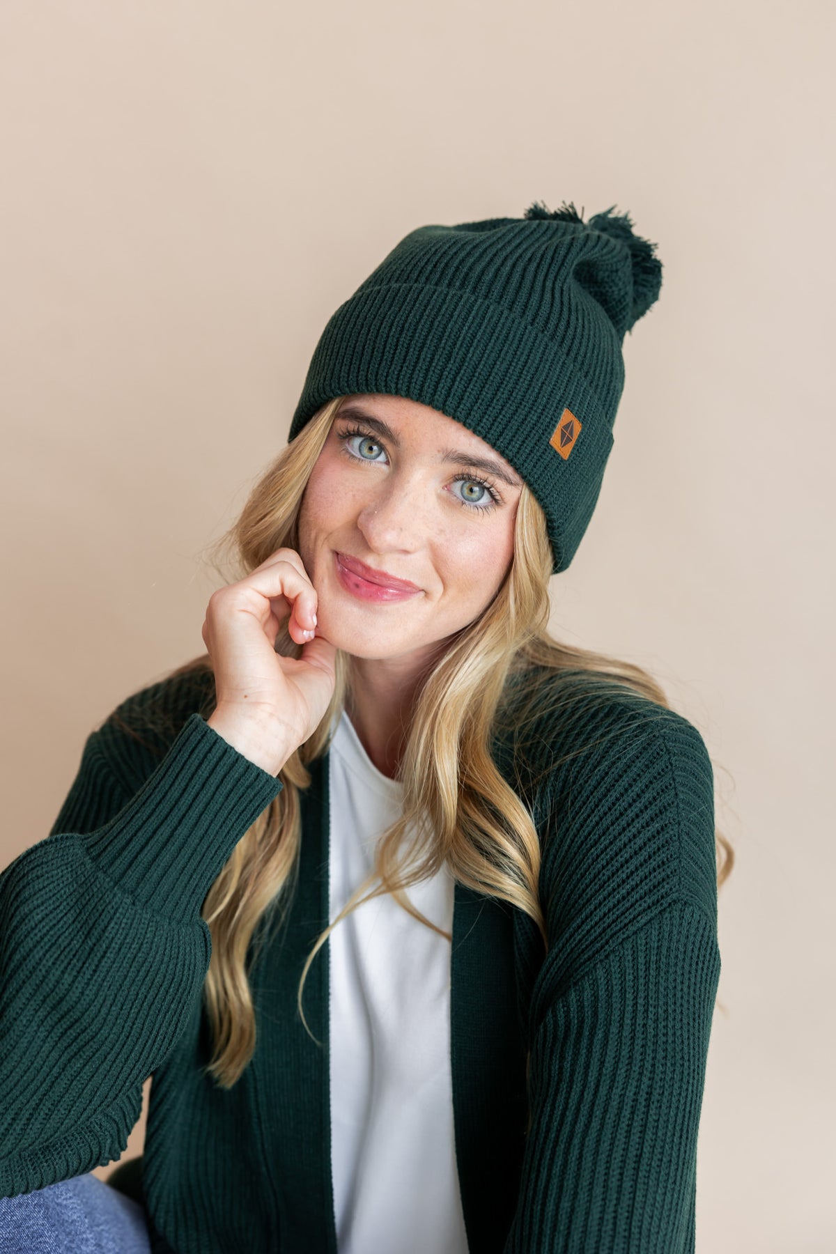 Modal wearing chunky knit adult ribbed beanie and chunky knit adult cardigan in cypress on a beige background
