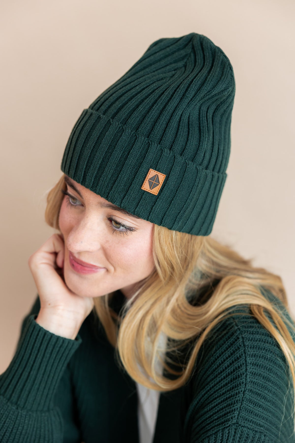 Modal wearing chunky knit adult ribbed beanie in cypress and chunky knit cardigan in cypress on a beige background