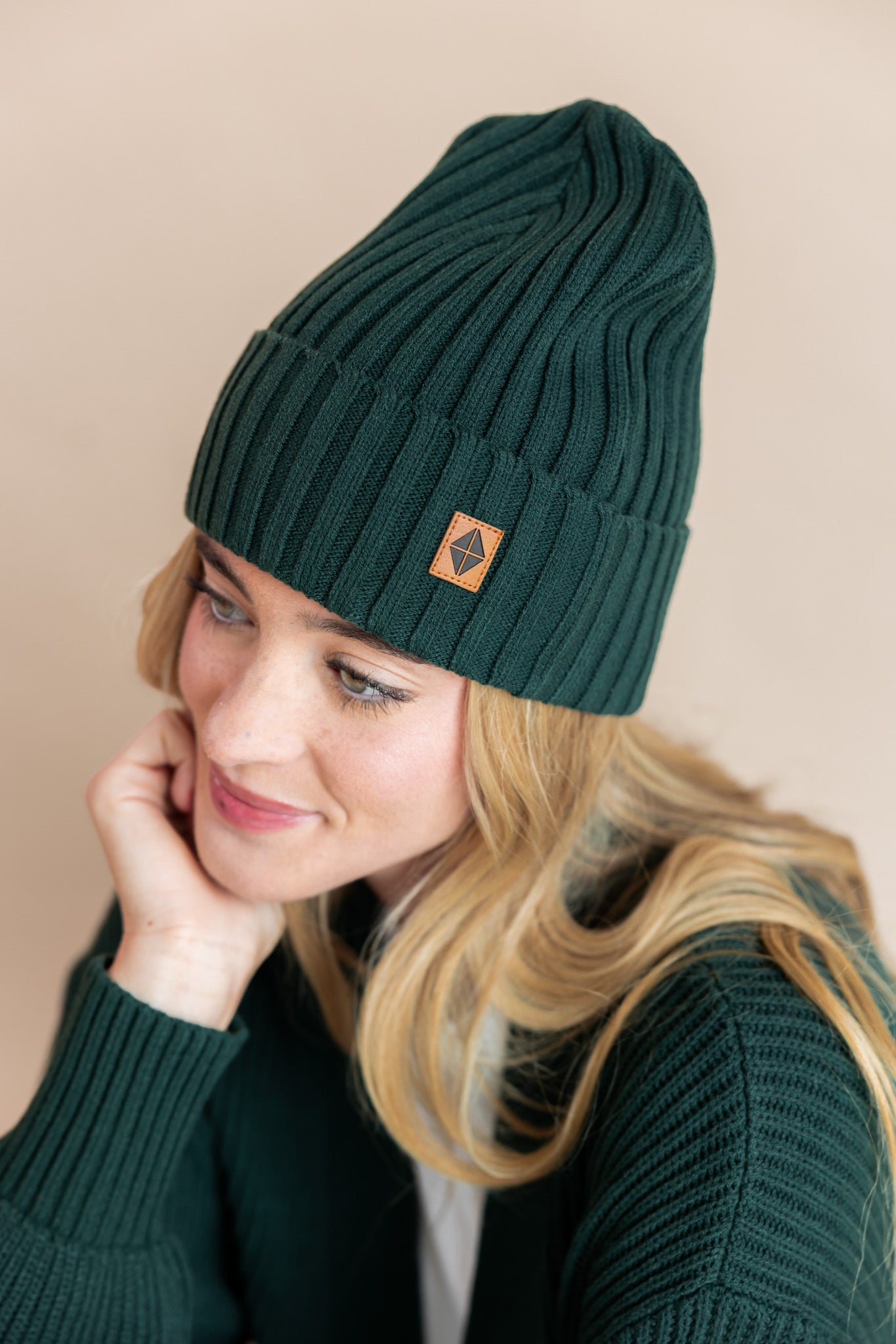 Modal wearing chunky knit adult ribbed beanie in cypress and chunky knit cardigan in cypress on a beige background