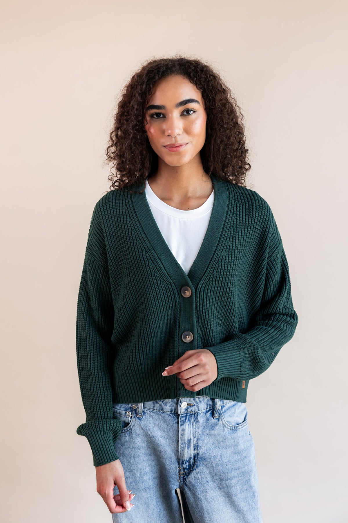 Modal wearing chunky knit cropped cardigan in cypress over white t-shirt and blue jeans on a beige background