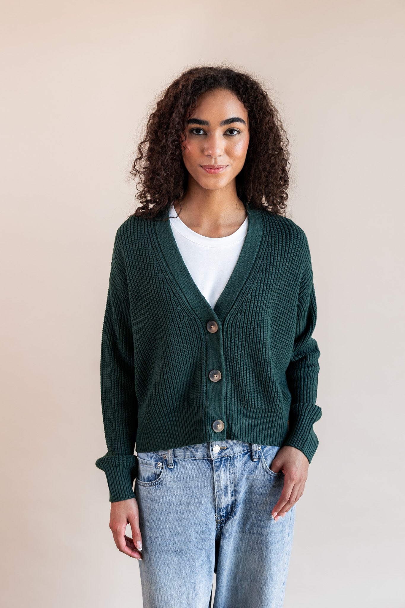 Modal wearing chunky knit cropped cardigan in cypress over white t-shirt and blue jeans on a beige background