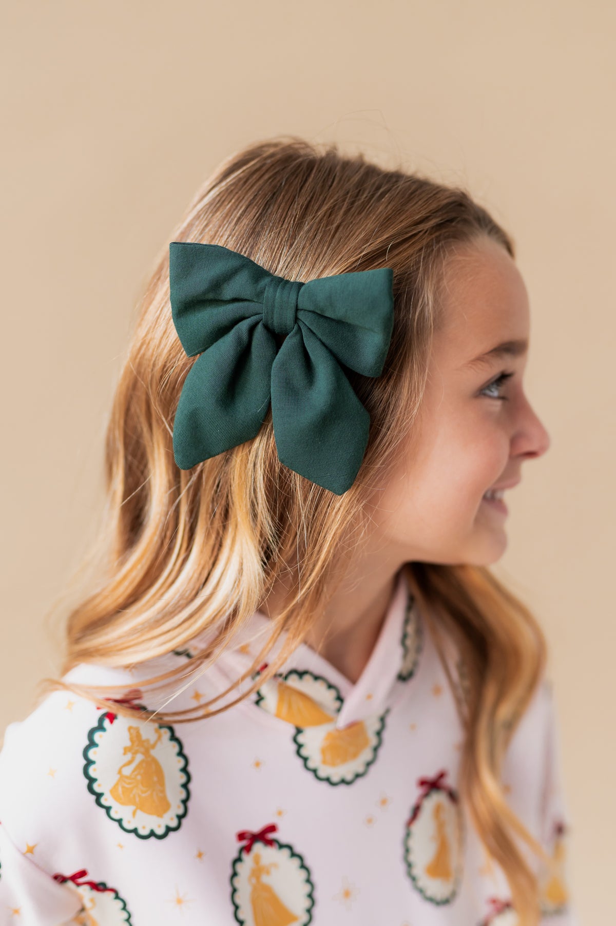 Girl wearing Medium Alligator Clip Bow in Cypress color in her hair on a beige background