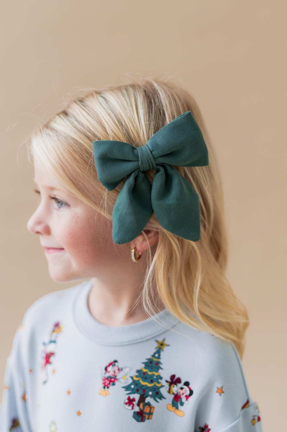 Girl wearing Medium Alligator Clip Bow in Cypress color in her hair on a beige background